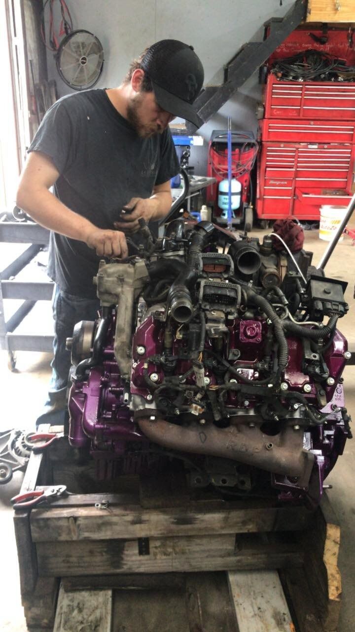 A man is working on a purple engine in a garage.
