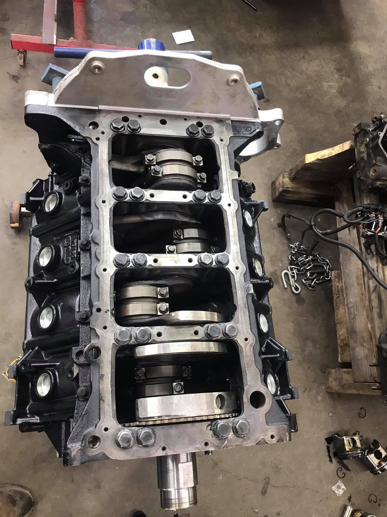 A block of a car engine is sitting on the ground in a garage.