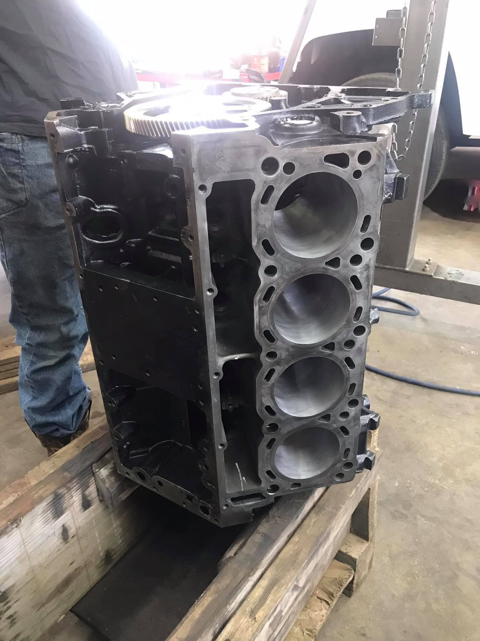 A block of a car engine is sitting on top of a wooden pallet.