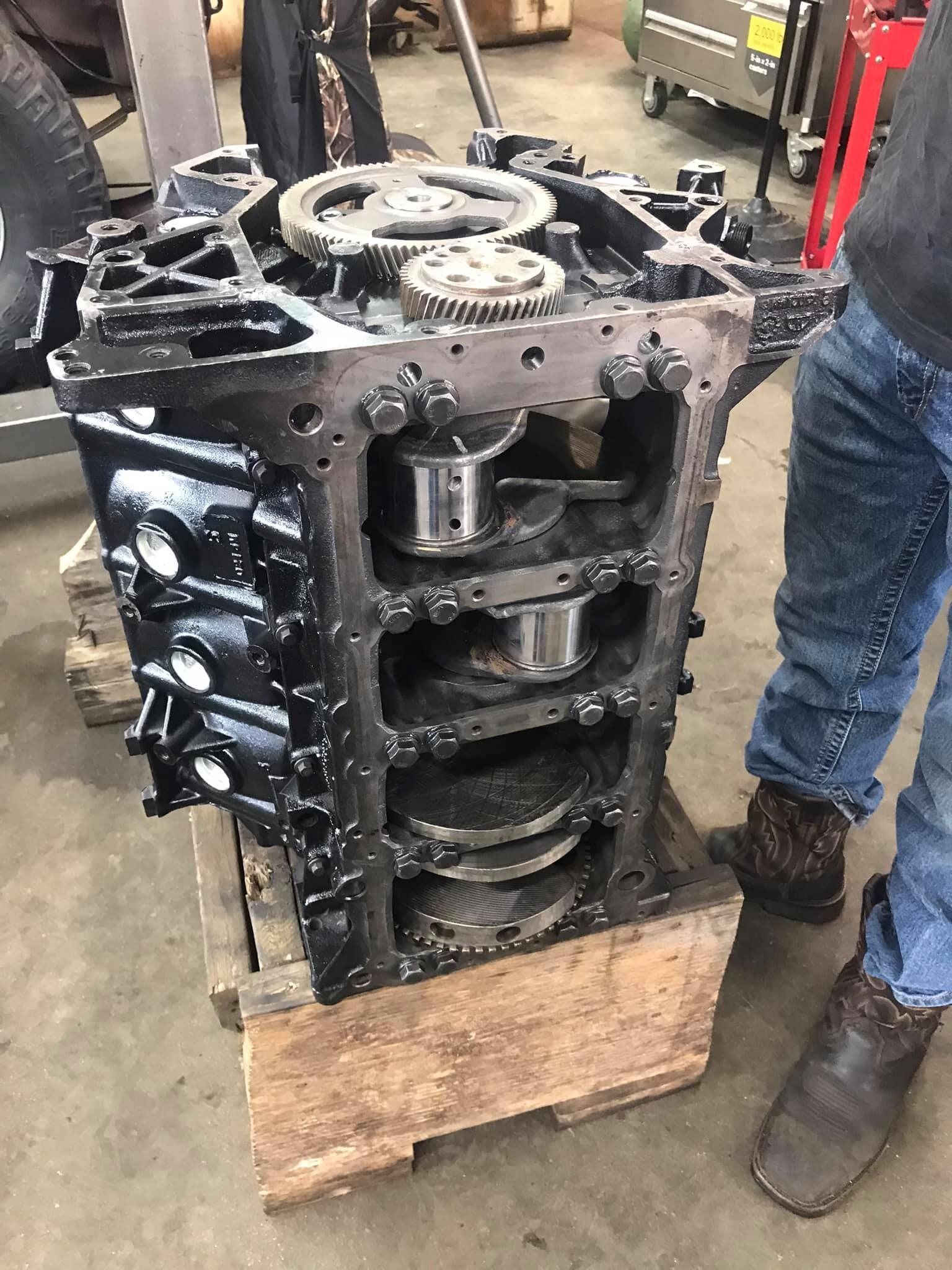 A man is standing next to a large engine block on a wooden pallet.
