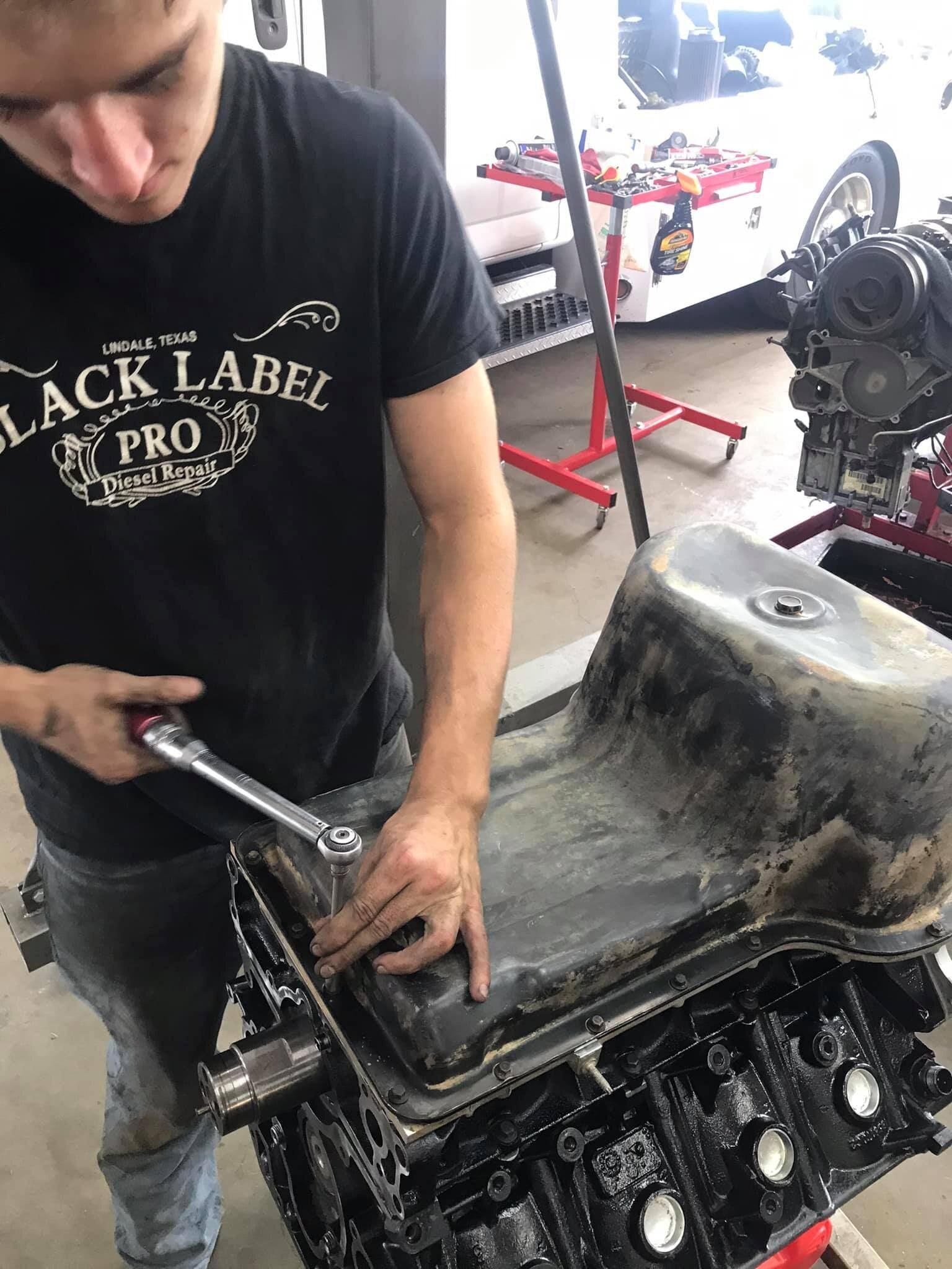 A man wearing a black label shirt is working on a car engine.
