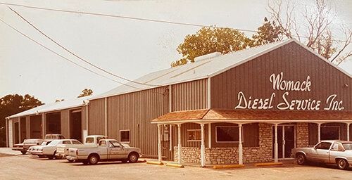 A row of cars are parked in front of a building that says wemack diesel service inc.