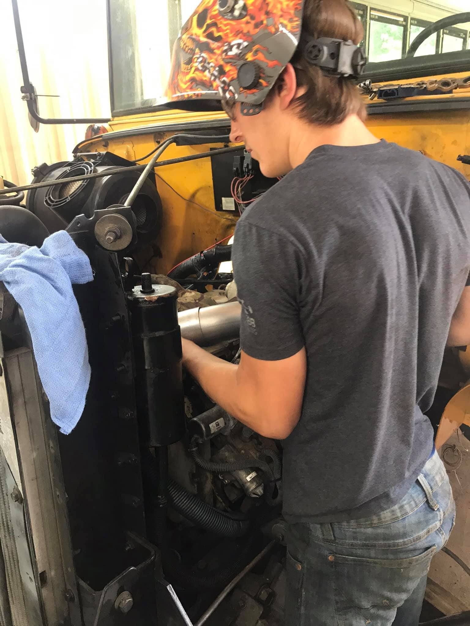 A man wearing a welding mask is working on a vehicle.