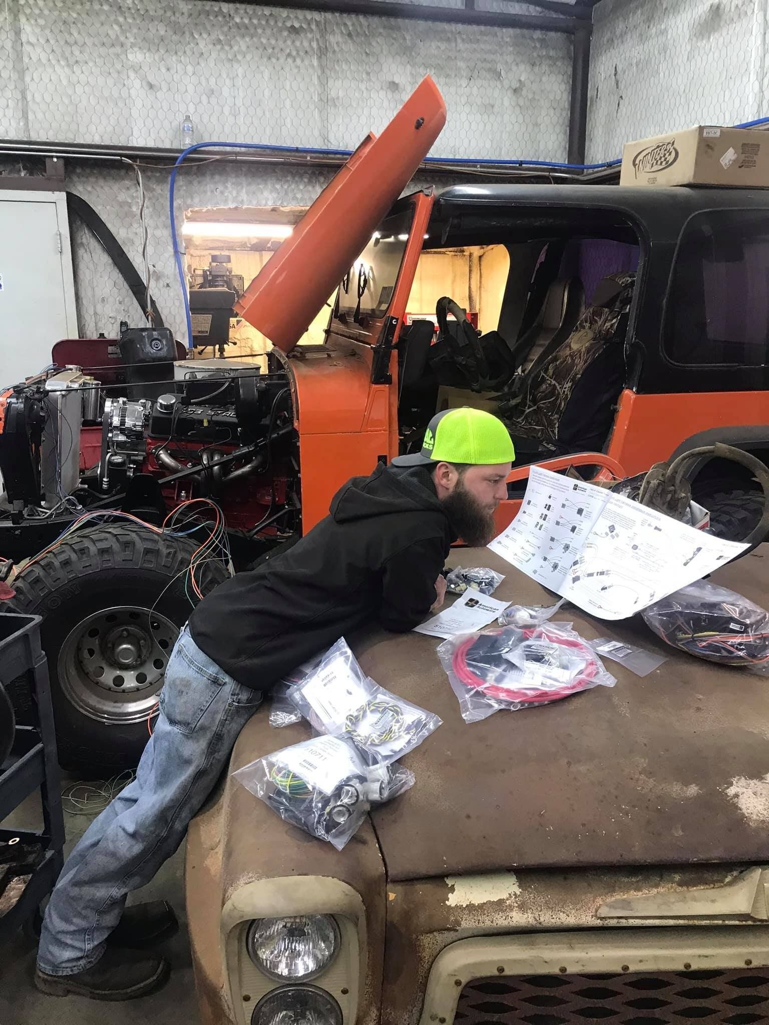 A man is kneeling on the hood of a truck in a garage.