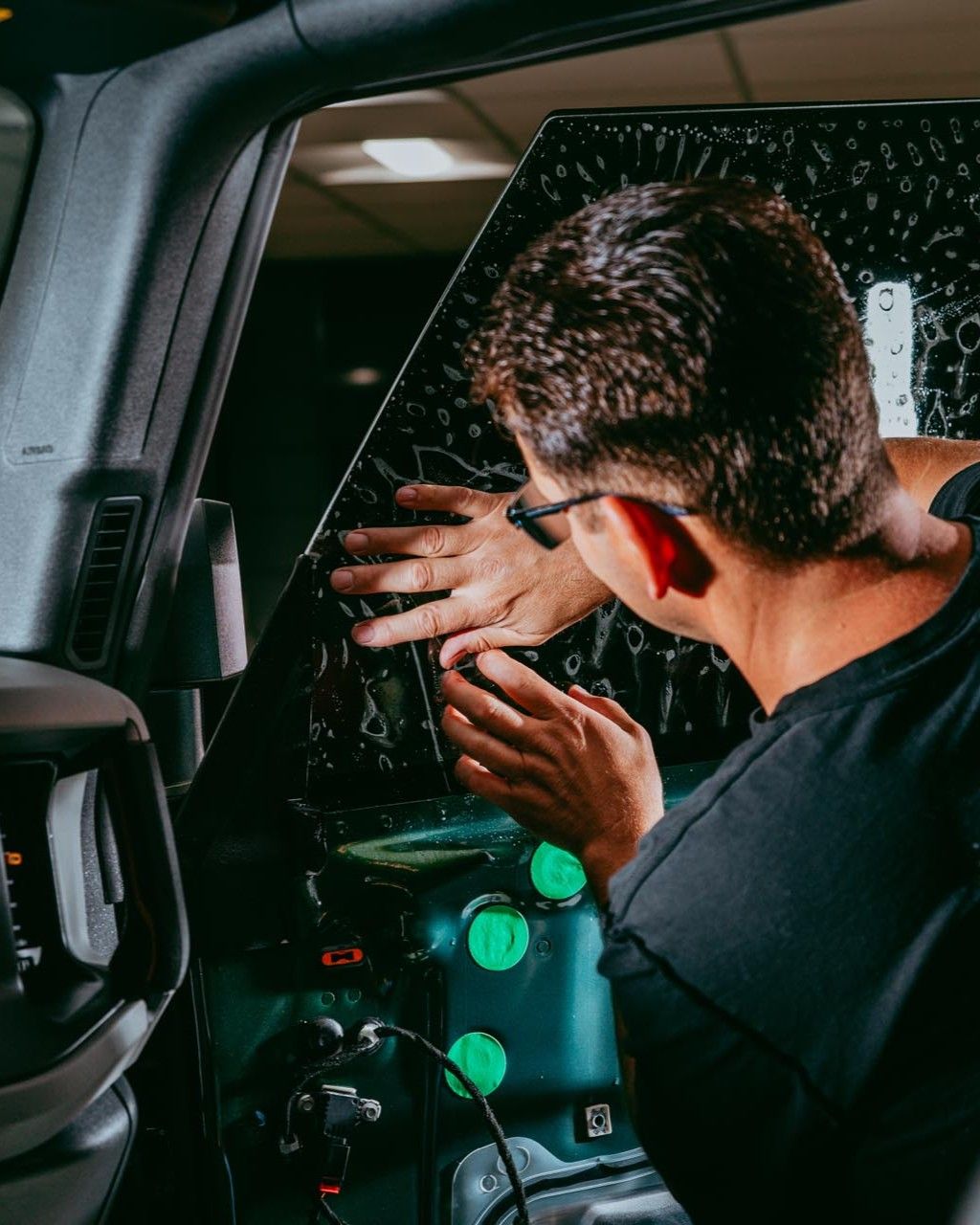 Man applying tint to a car window. He is wearing glasses and is focused on his work inside a vehicle.