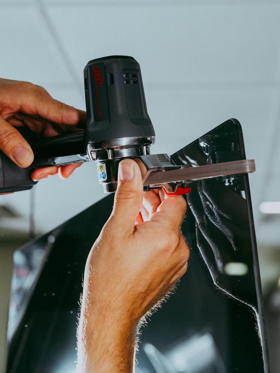 Person using a power tool with a sanding attachment to smooth a black surface, possibly for car detailing.