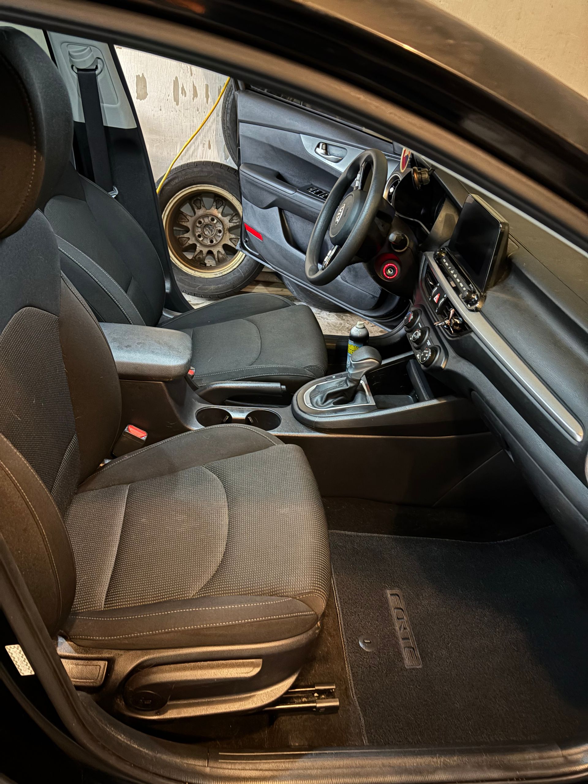Interior car view, black seats, steering wheel, opened door showing a spare tire.