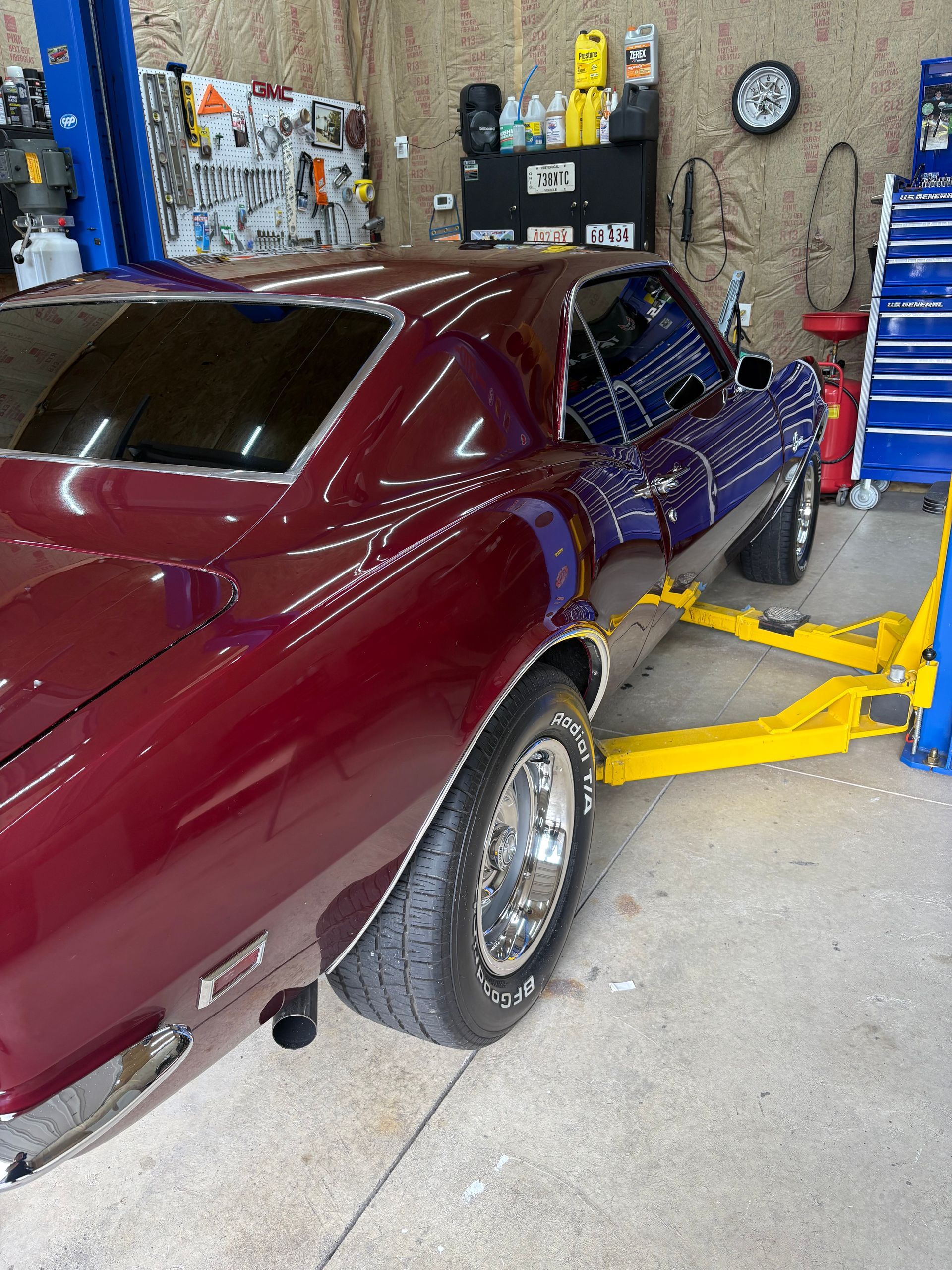A person in black gloves polishing a silver car with a red and black buffer in a well-lit garage.