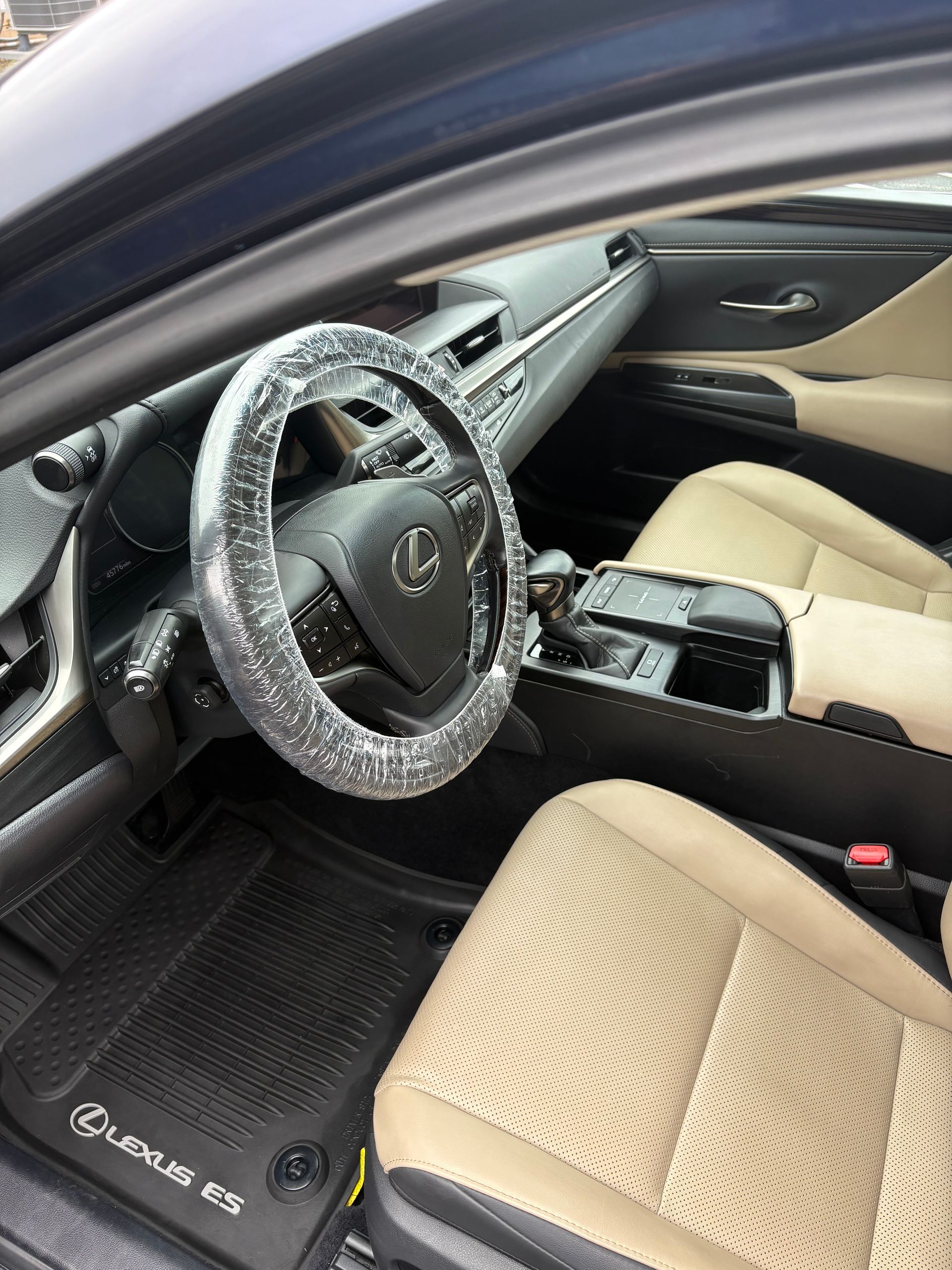 A person wearing a black glove wipes a dark car door panel with a gray cloth, the vehicle's red frame visible.