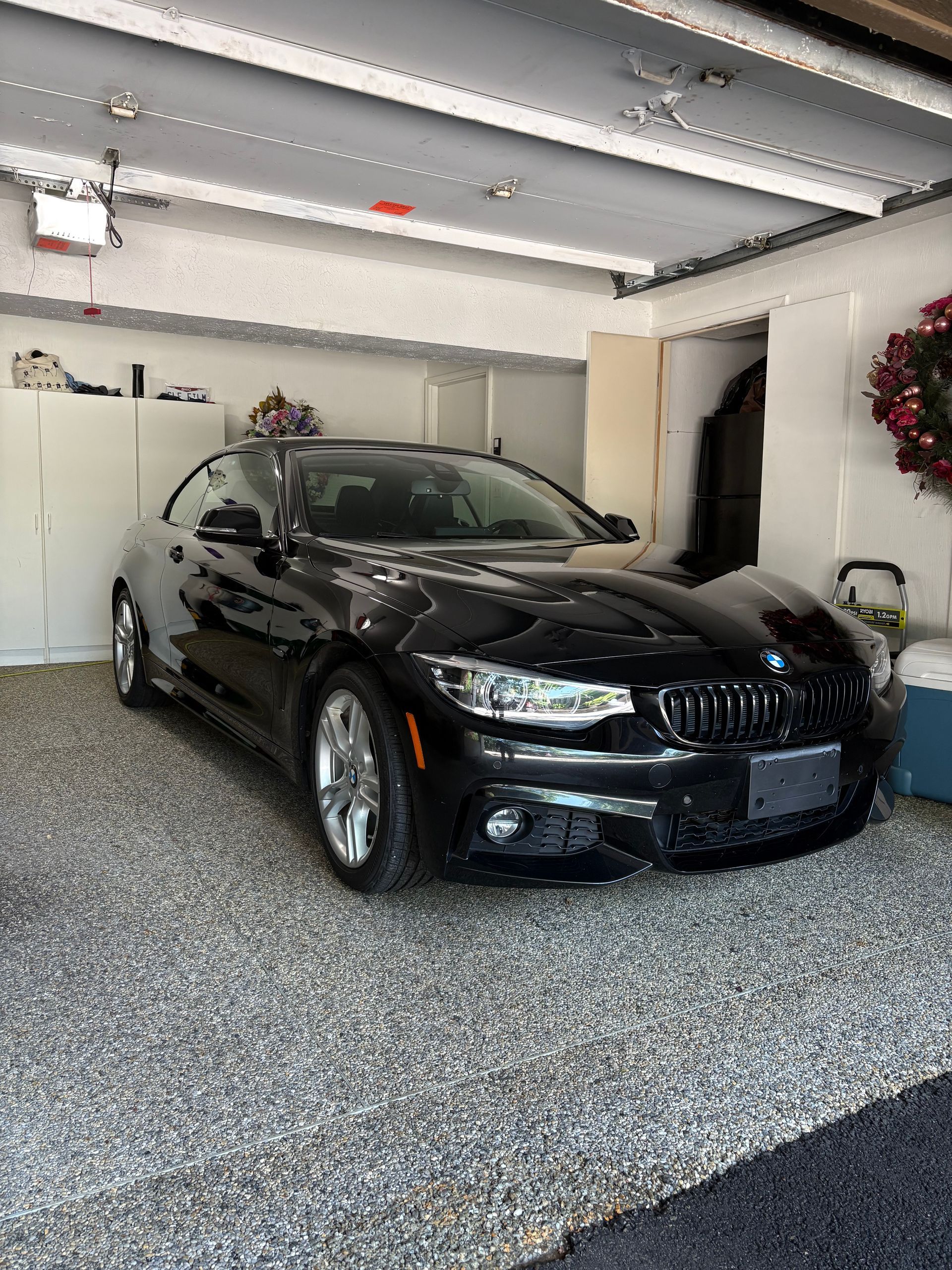 Black BMW coupe parked inside a garage with gray speckled flooring and white cabinets.