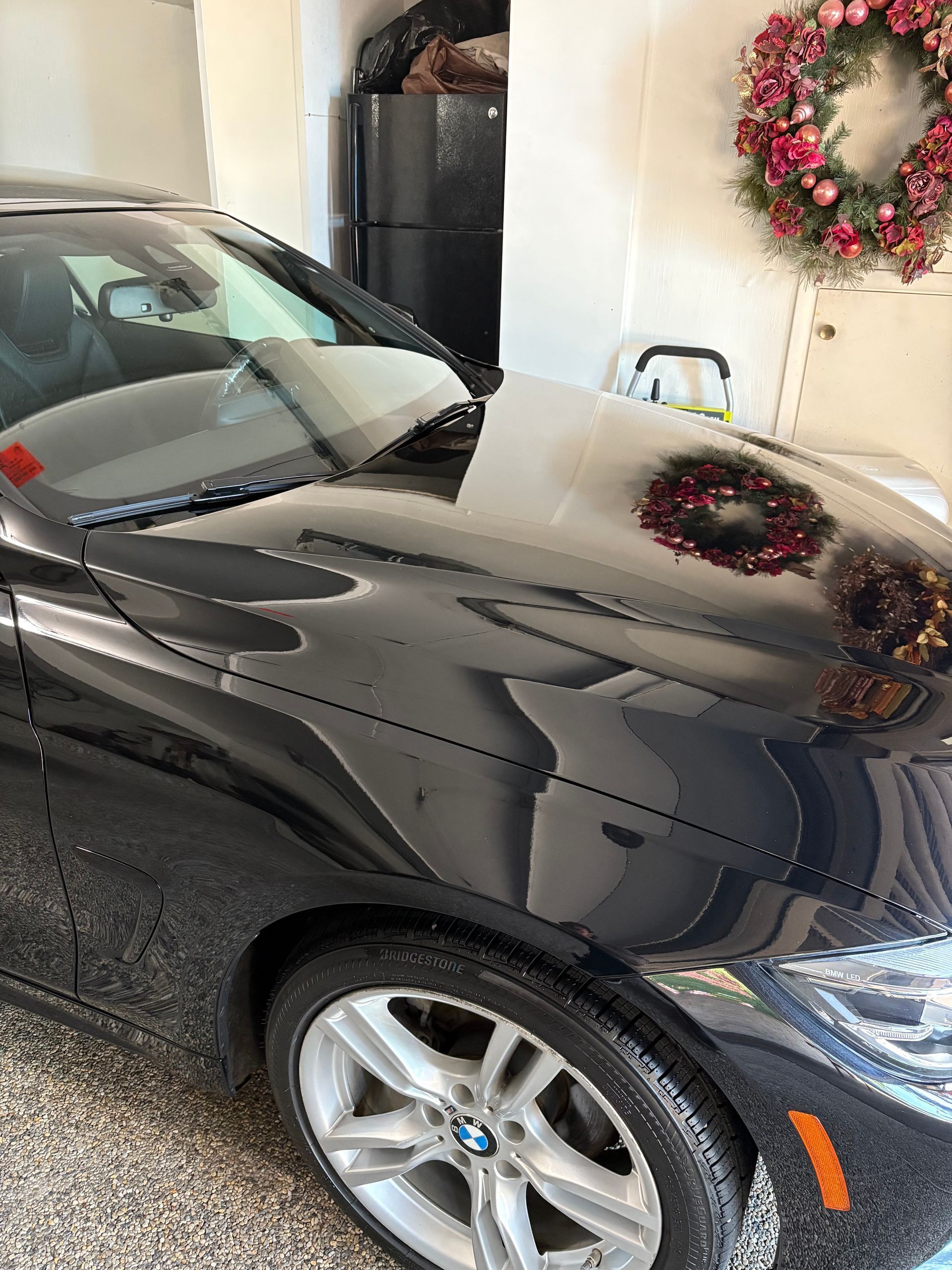 Person in black gloves applying liquid to a car panel with a cloth, indoors.