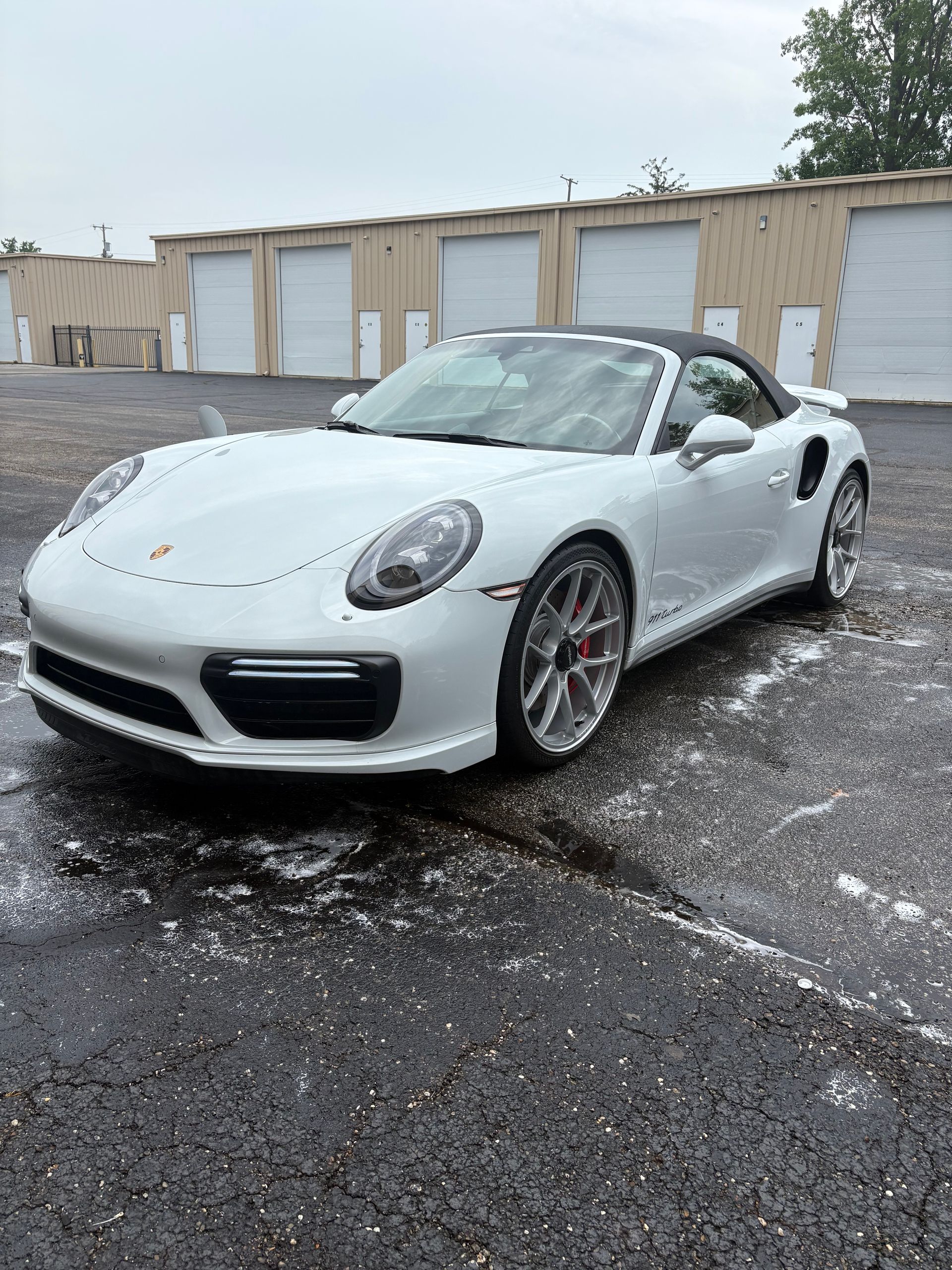 White Porsche convertible parked on wet asphalt. Building background.