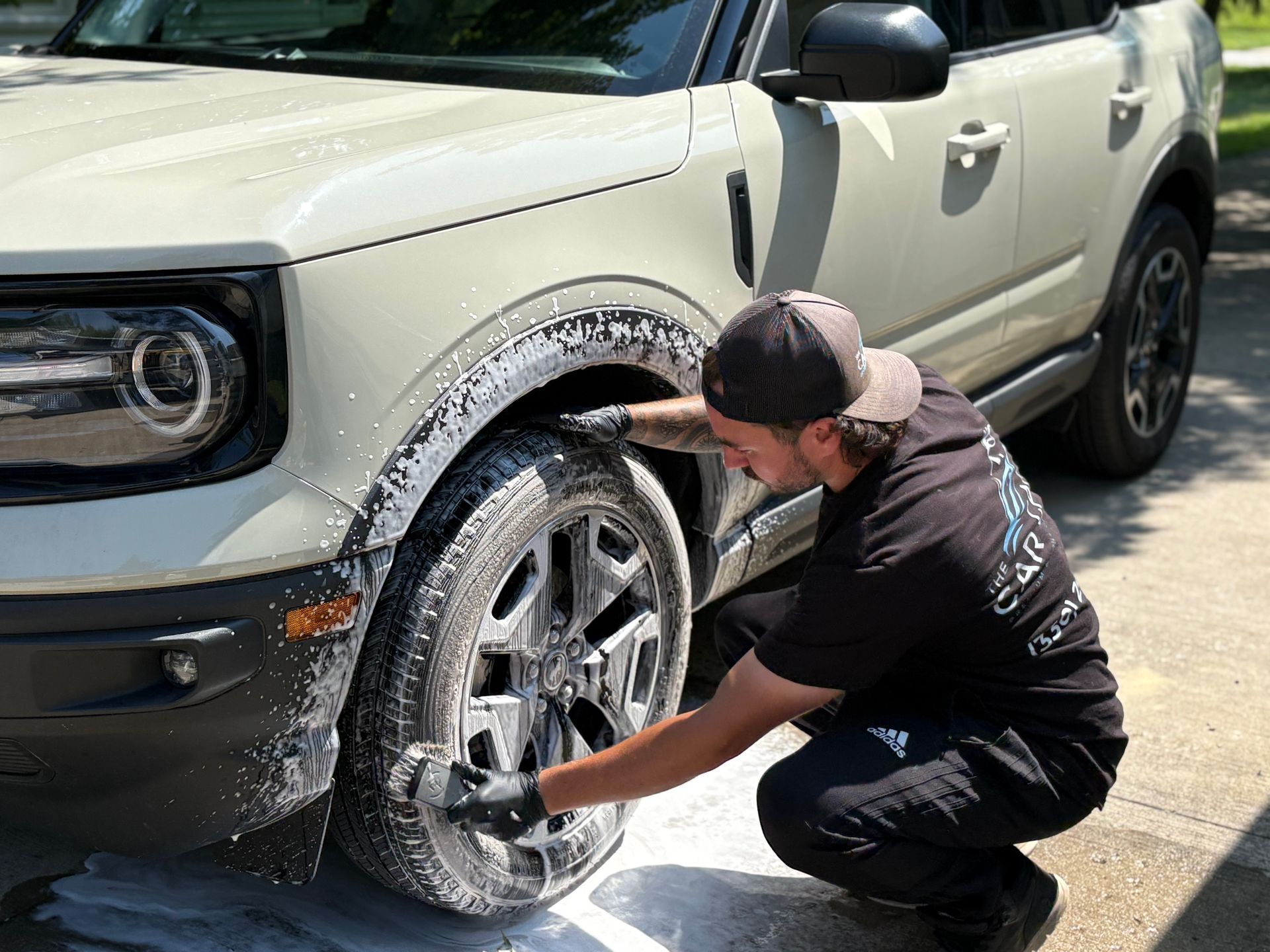 Man polishing a white car in a garage. He wears a headlamp, gloves, and sits on a stool.