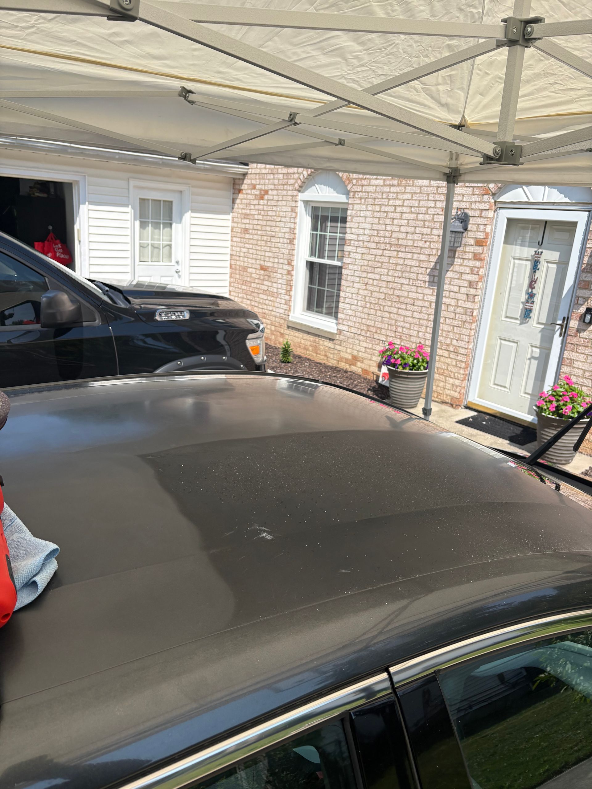 Black car roof with dirt under a tent, brick building in the background.