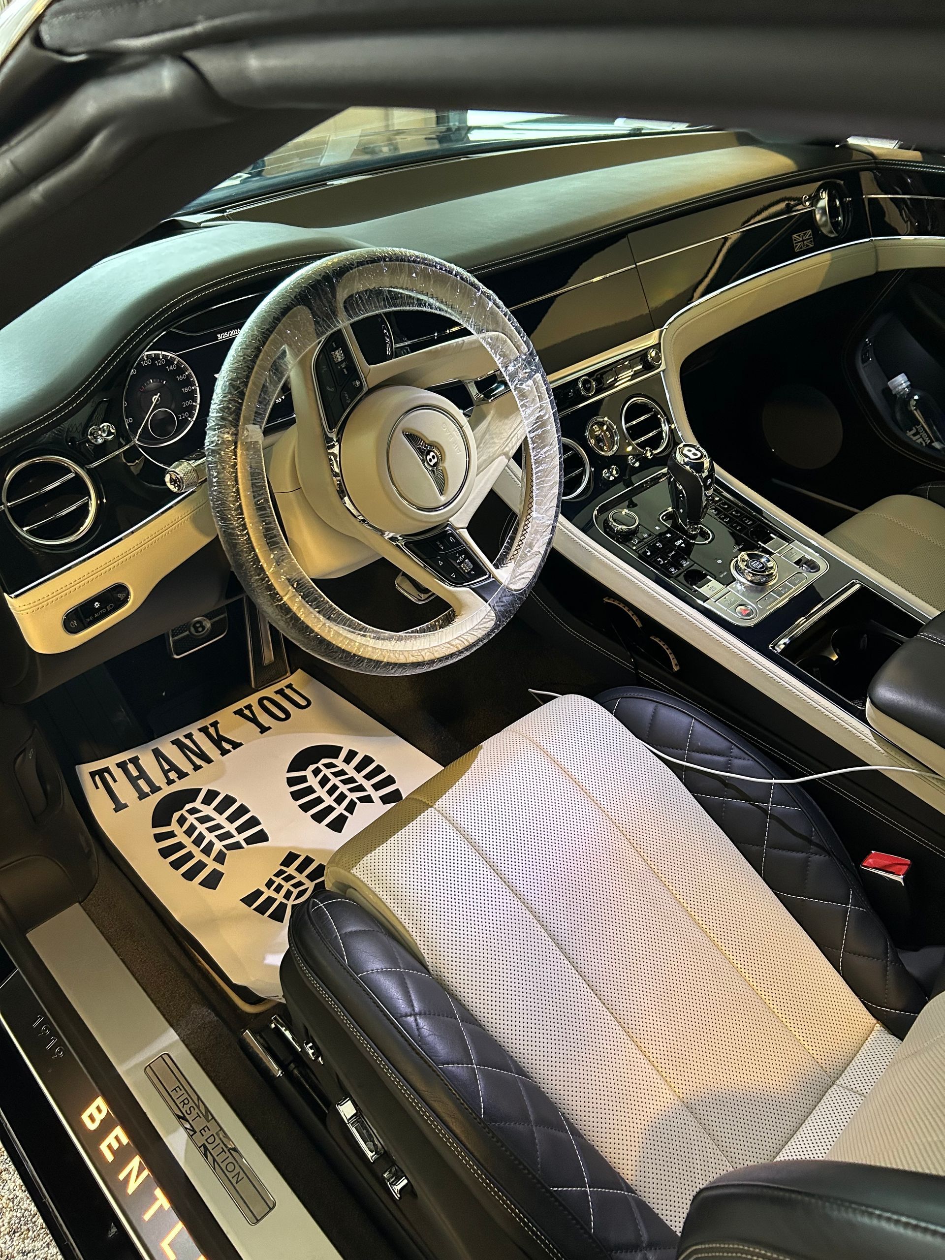 Interior of a black Lexus car, driver's side. Steering wheel covered in plastic. Black leather seats.