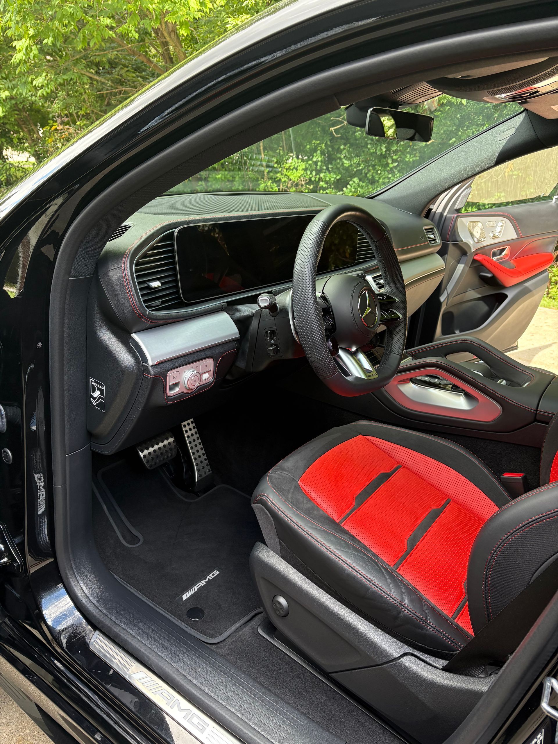 Interior shot of a black and red sports car seat. The focus is on the driver's seat, with sporty stitching and metallic accents.