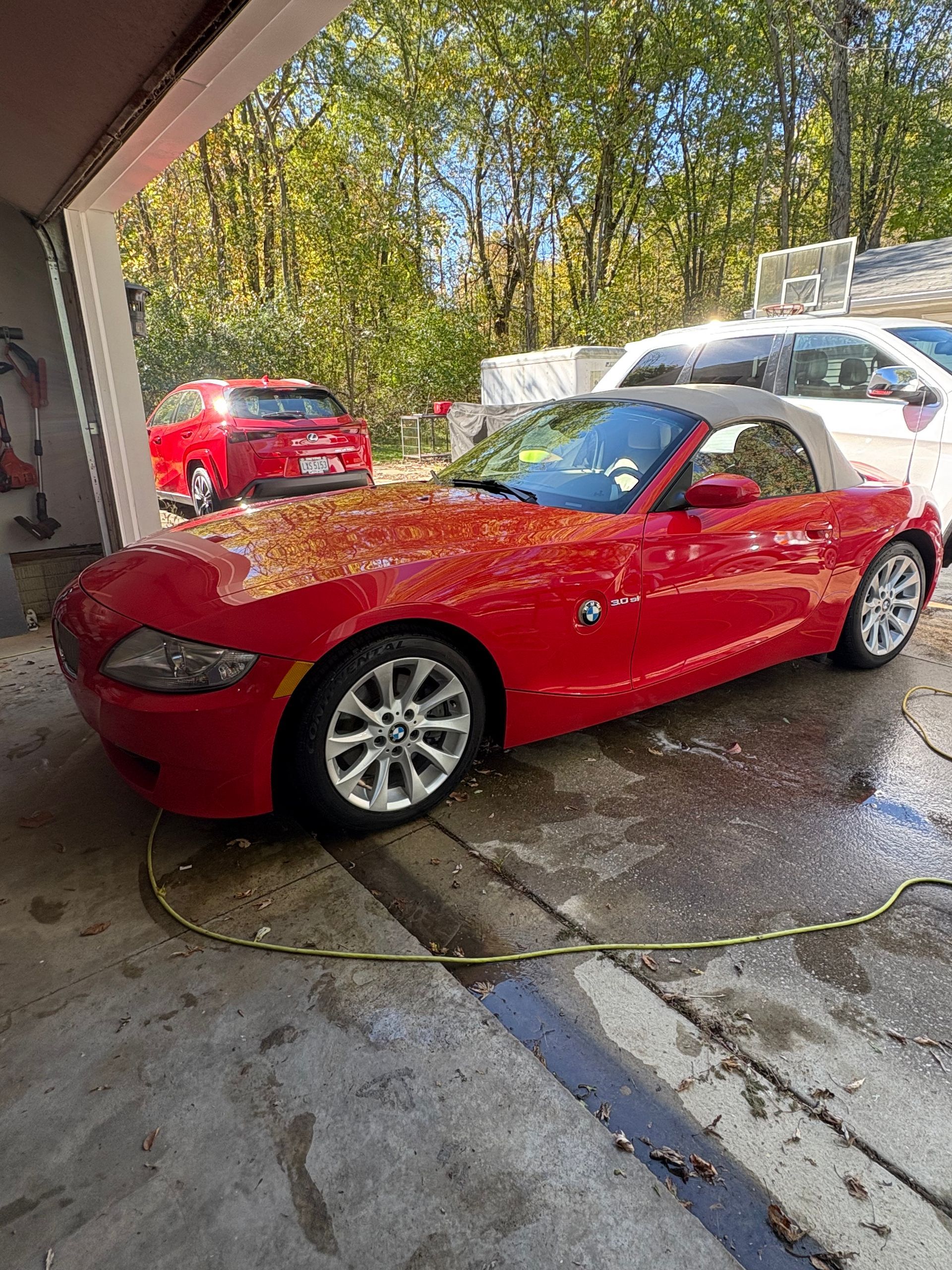 Gloved hands applying liquid from a bottle onto a microfiber applicator pad in front of a blue car.