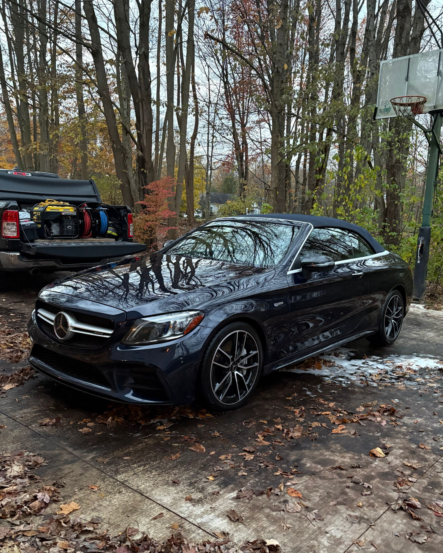 Dark blue Mercedes-Benz convertible being washed outdoors, surrounded by trees and a basketball hoop.