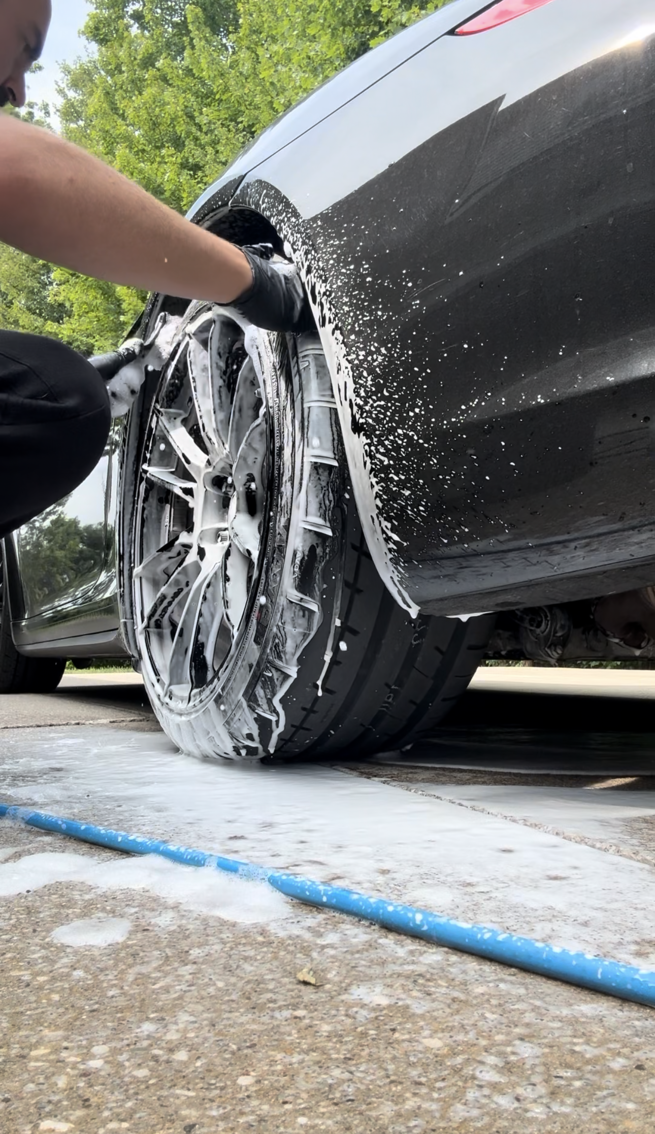 Person washing a car tire and rim with a soapy sponge on green grass.