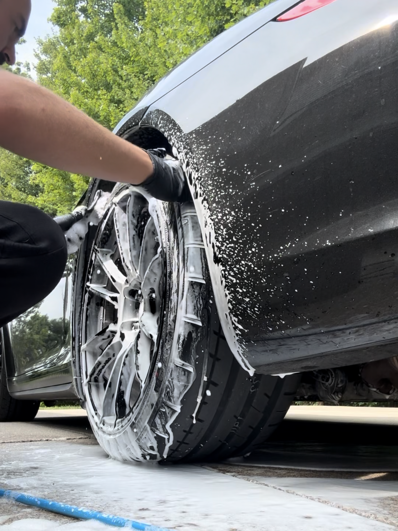 Person washes black car tire with soapy foam.