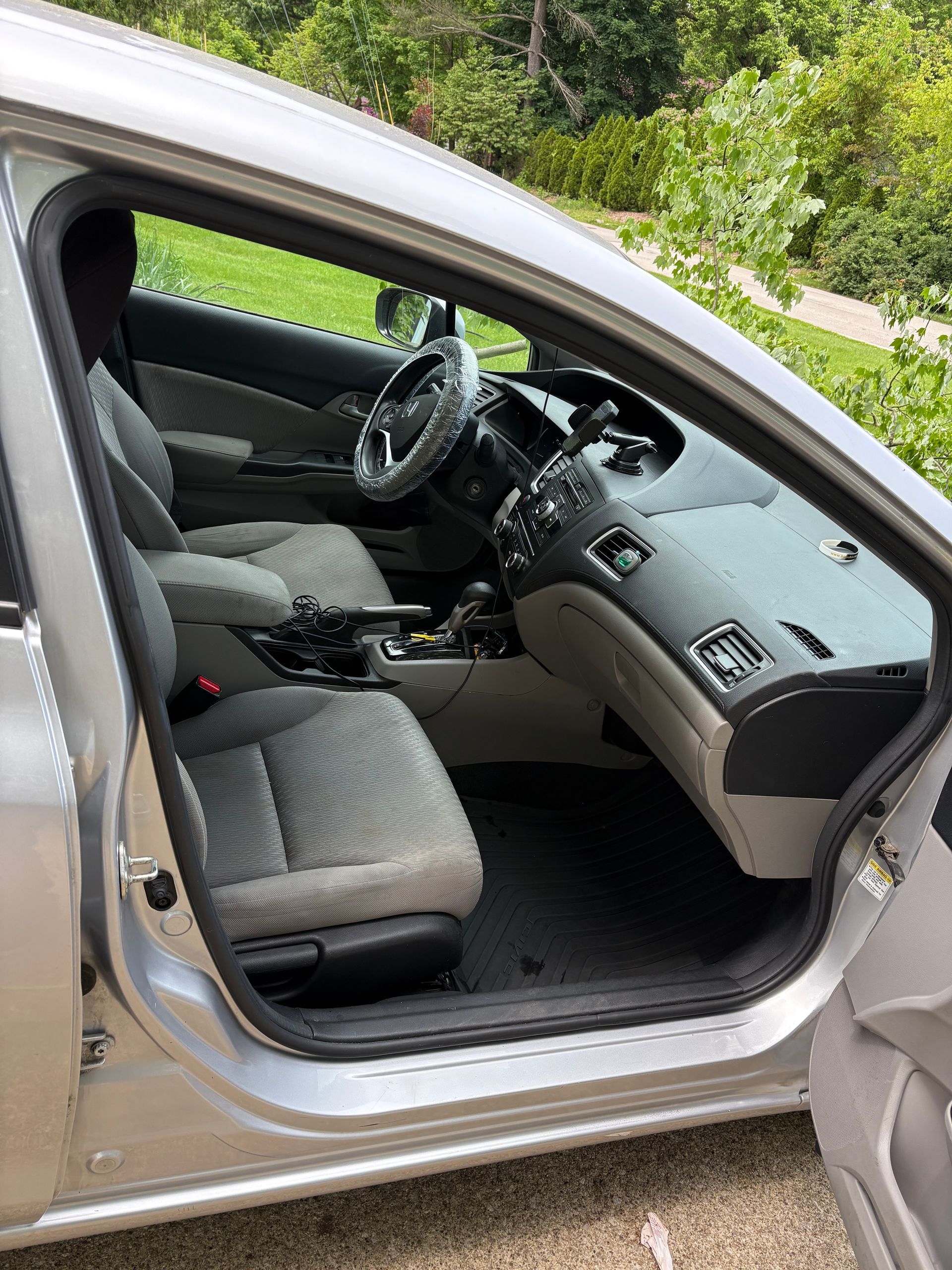 Silver car's open driver-side door reveals light grey interior with seats, steering wheel, and dashboard.