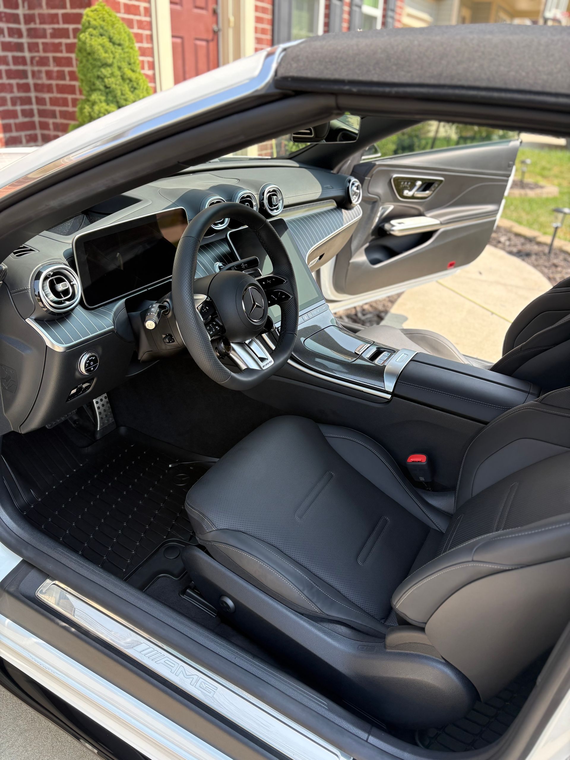Inside of a modern, open-top sports car with black leather seats and a black and gray interior.