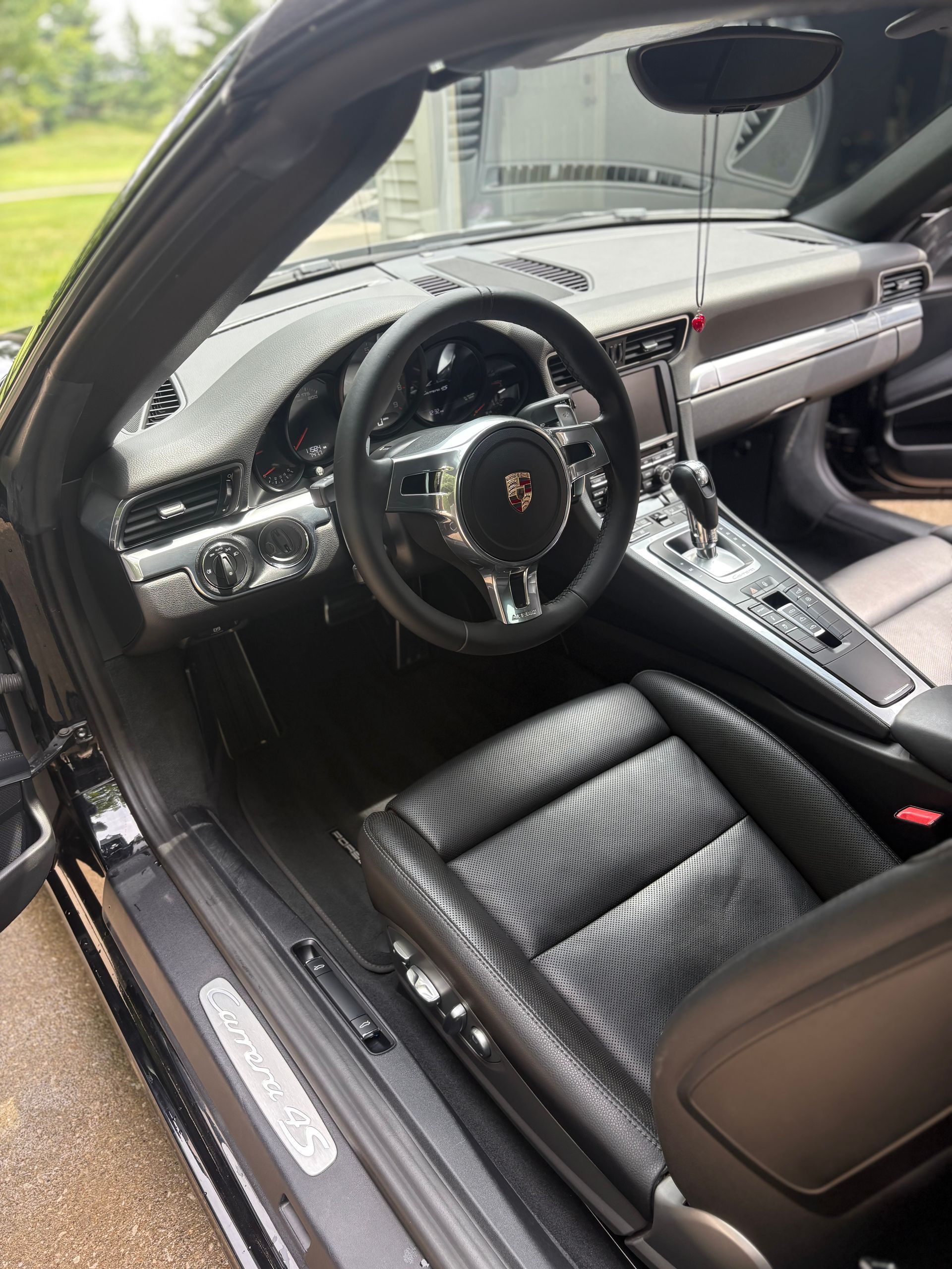 Black Porsche 911 interior: leather seats, chrome accents, steering wheel, dashboard. Open door, outdoors.