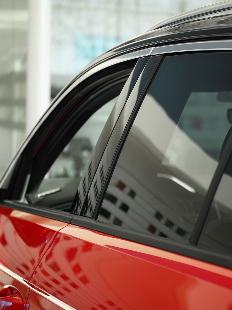 Close-up of a red car with tinted windows, reflecting a building. Black trim accents the window frame and roof.