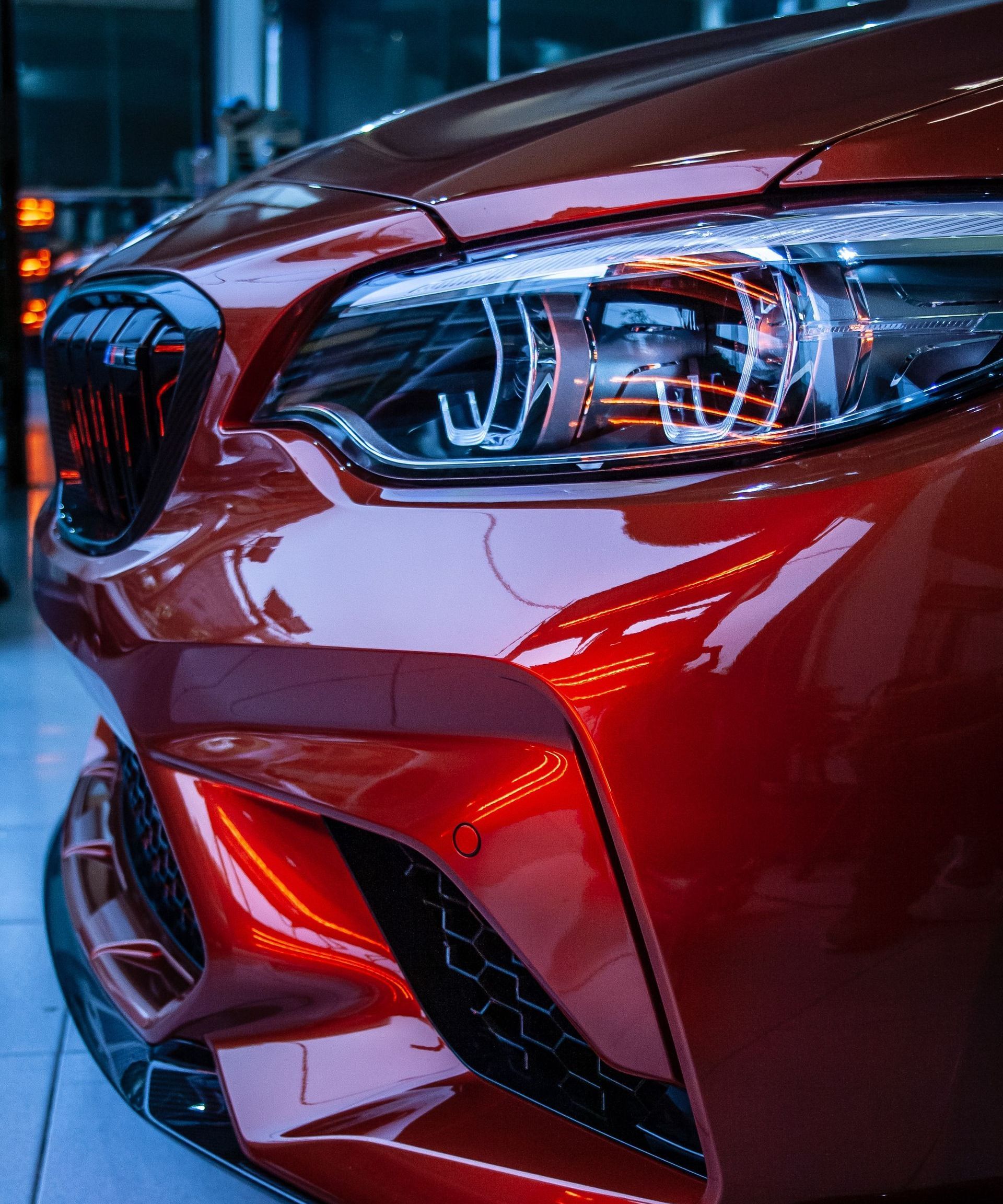 Close-up of a shiny, red sports car's front, showcasing its headlights and grill.