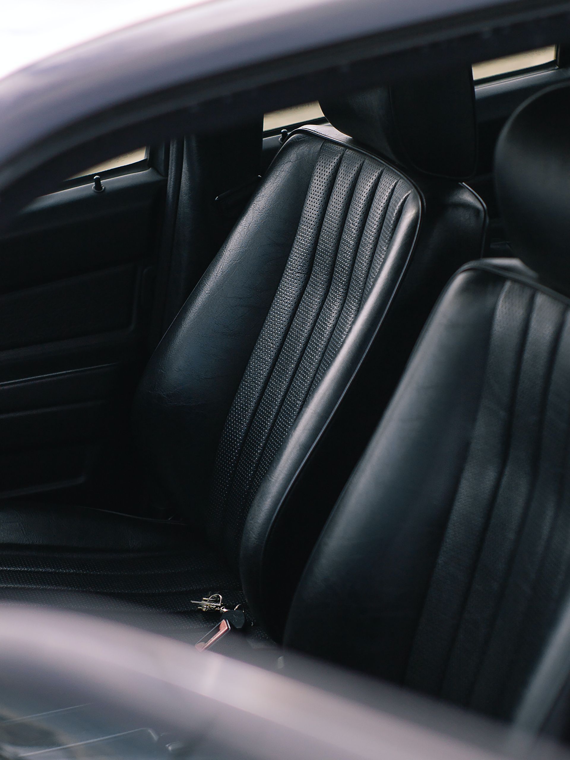 Black leather car seats, showing vertical stitched detailing. The setting is inside a vehicle.