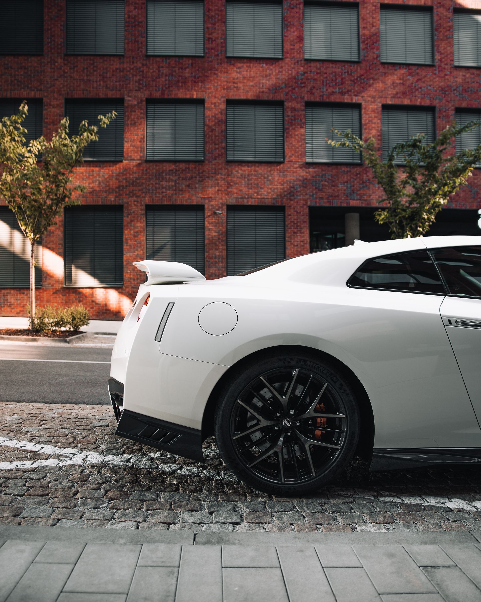 White Nissan GT-R parked on a brick-lined street in front of a red brick building.