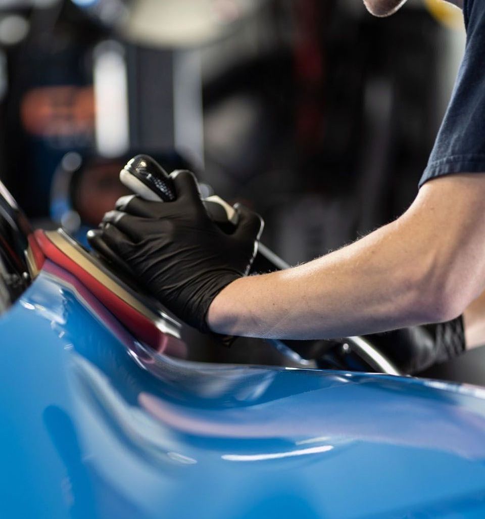 Person wearing black gloves polishes a blue car with an electric buffer in a shop.