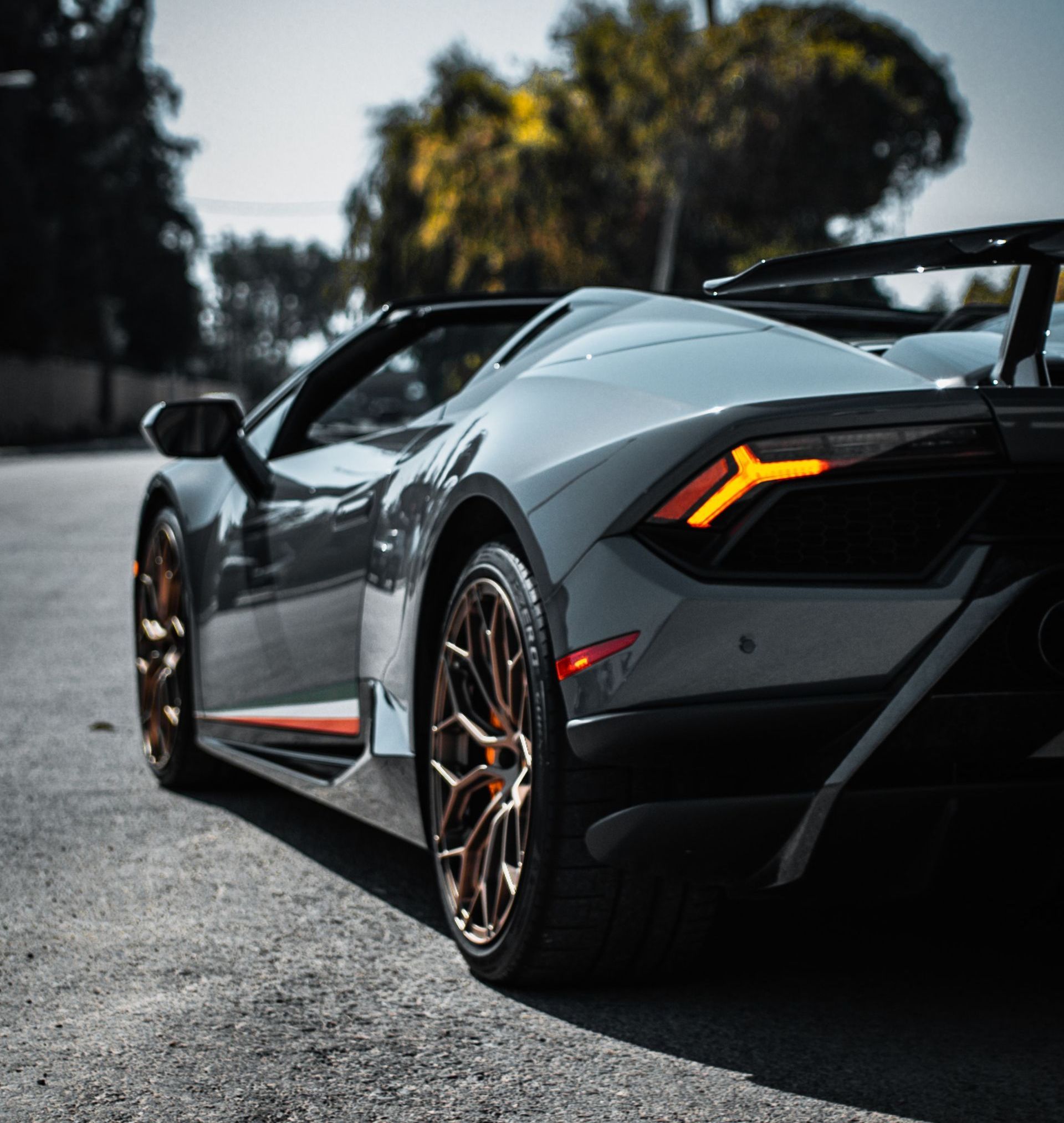 Gray Lamborghini convertible parked on an asphalt road, showcasing bronze-colored wheels and an orange stripe.