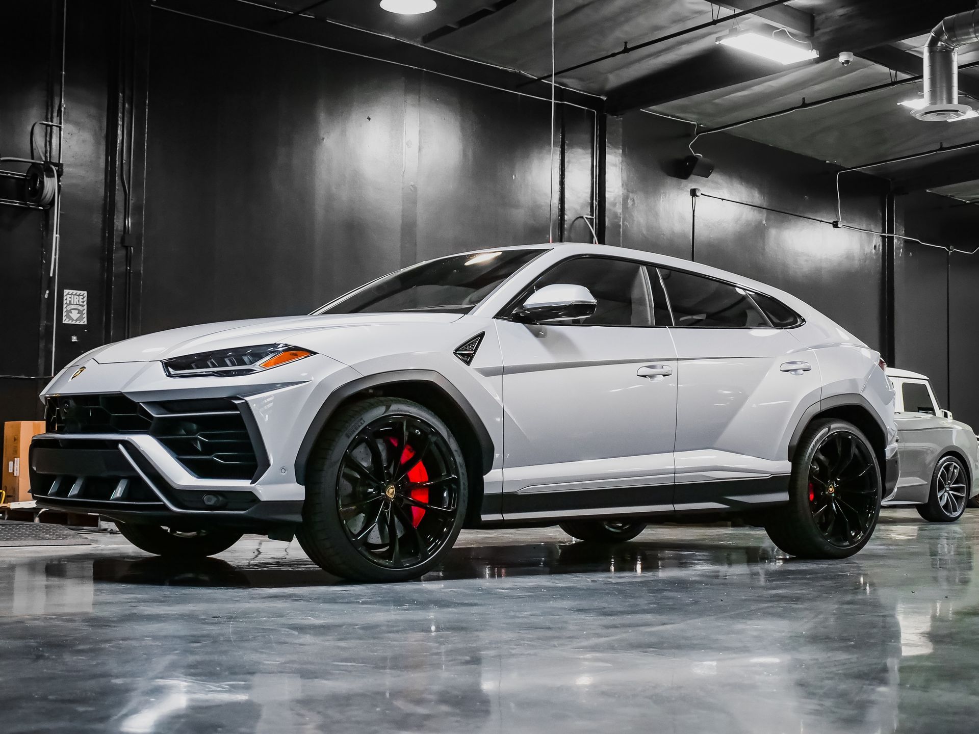 A white Lamborghini Urus SUV with black wheels and red brake calipers sits inside a dark garage.
