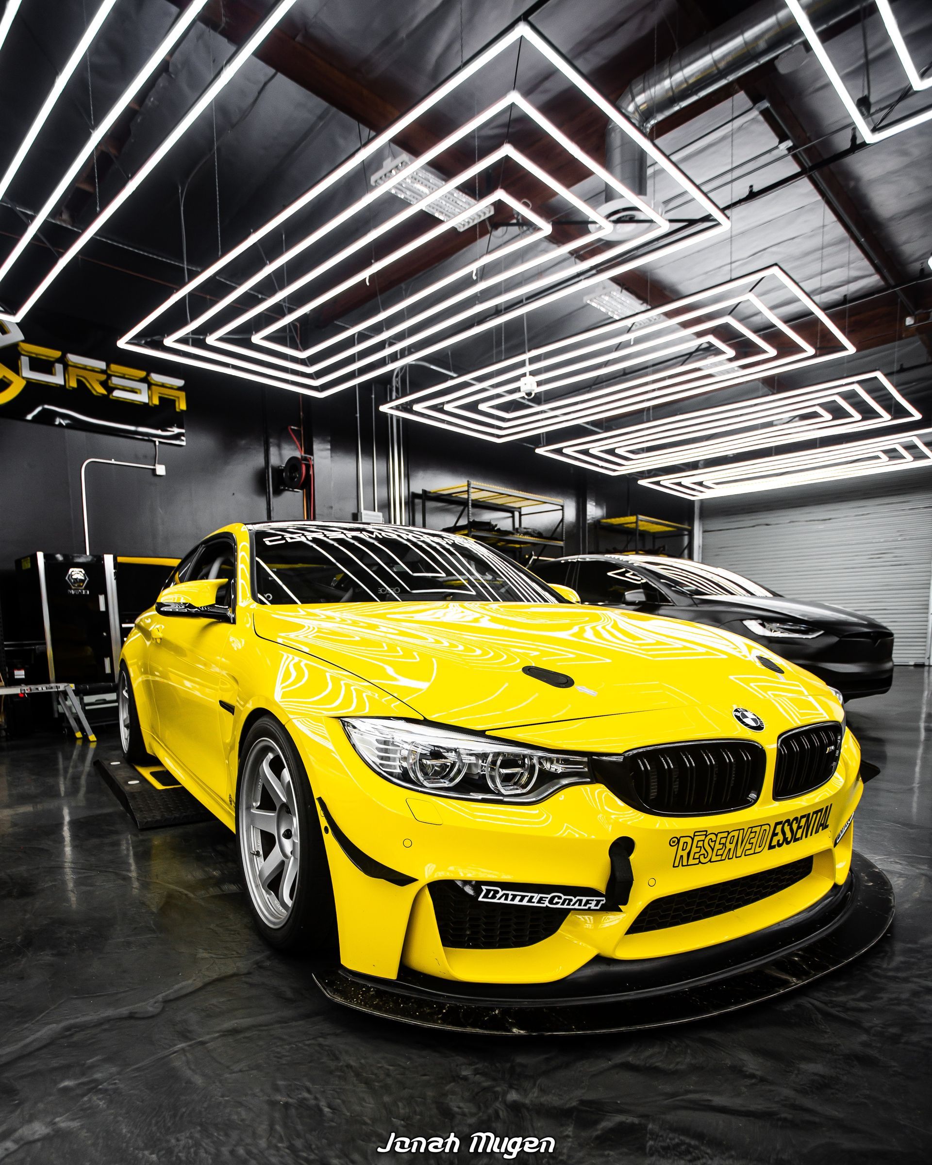 Yellow BMW sports car in a garage with bright neon lights, featuring a black front splitter and silver wheels.