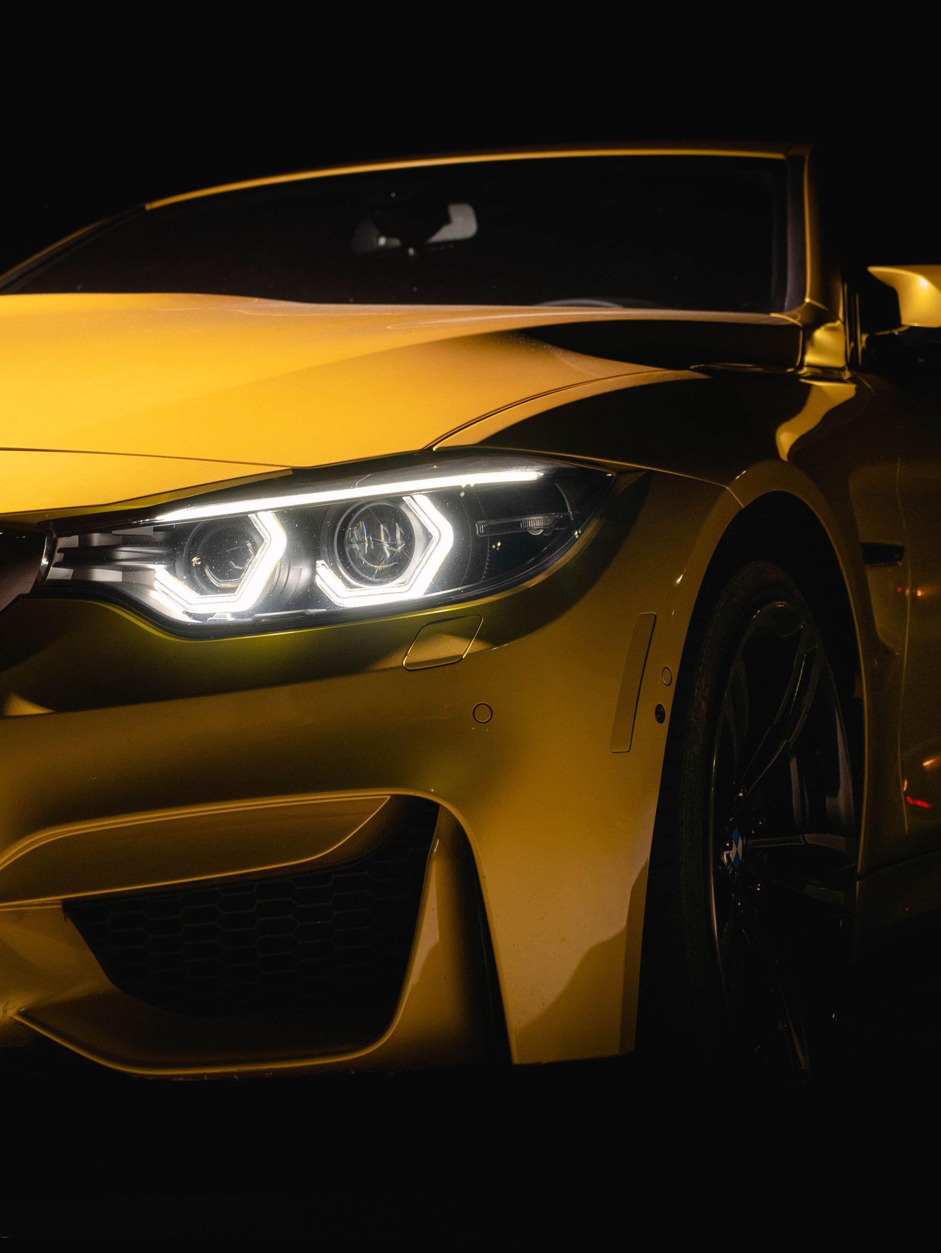 Yellow sports car with bright headlights against a dark background.