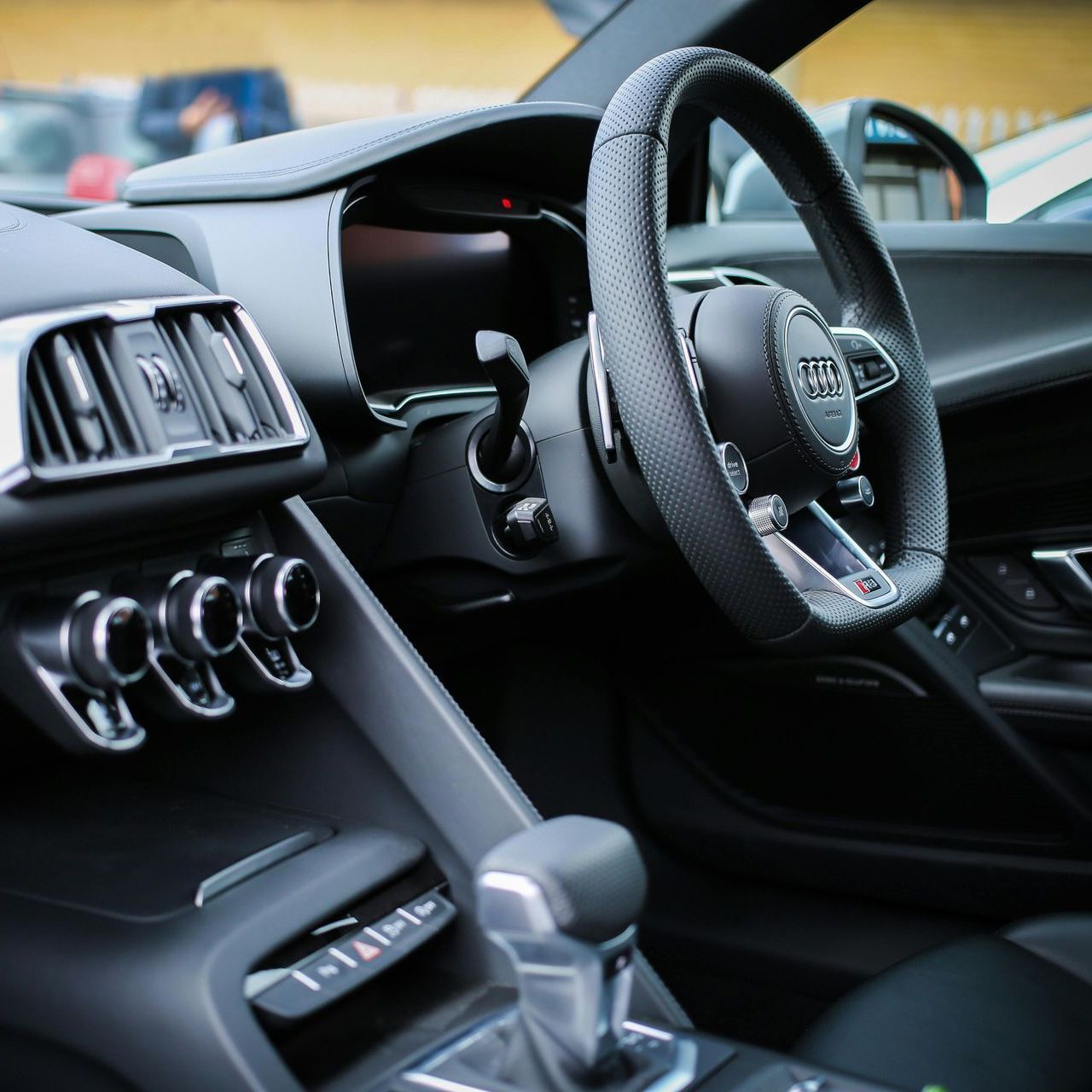 Interior view of a black Lamborghini, featuring a steering wheel, dashboard, seats with orange accents.