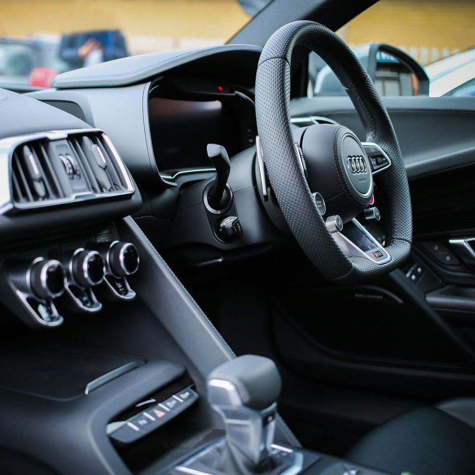 Interior view of a black Lamborghini, featuring a steering wheel, dashboard, seats with orange accents.