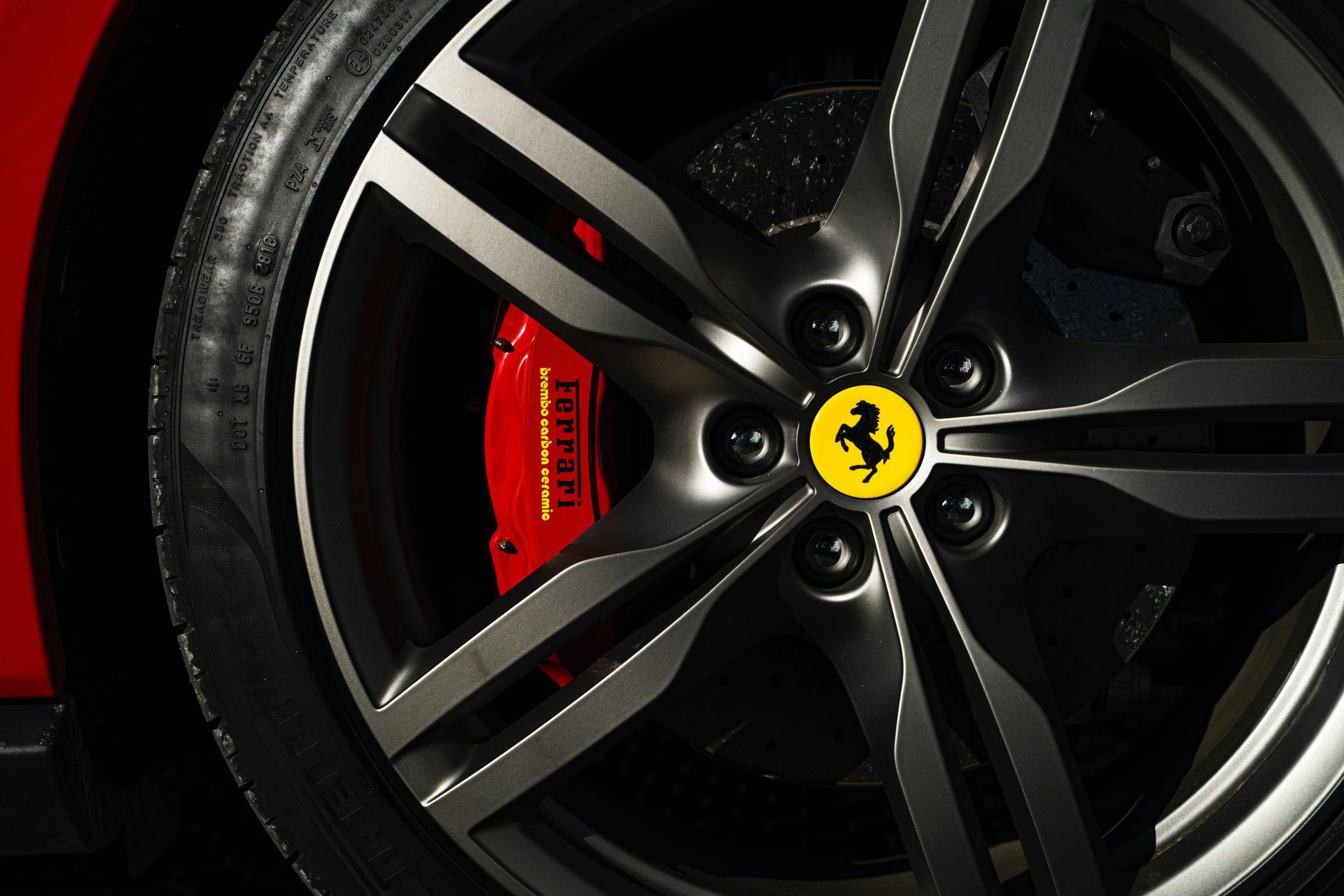 Close-up of a Ferrari car wheel with a red brake caliper, black tire, and a yellow Ferrari logo on a grey rim.