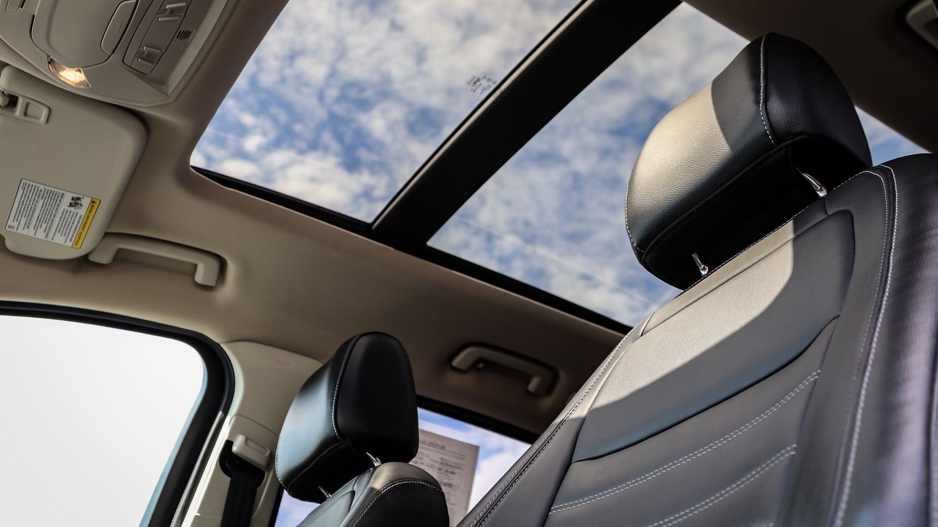 Interior car view with open sunroof, showing blue sky and black leather seats.