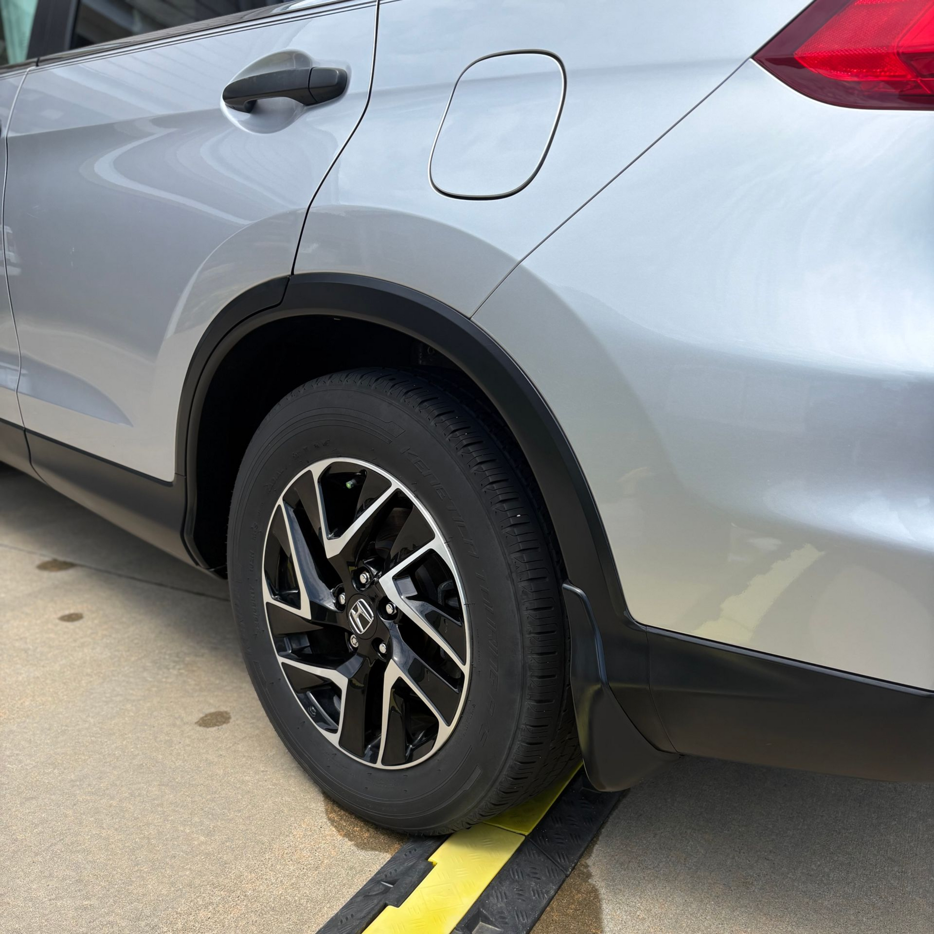 Silver car's rear side view with black fender, black and silver rim, and black mud flap.