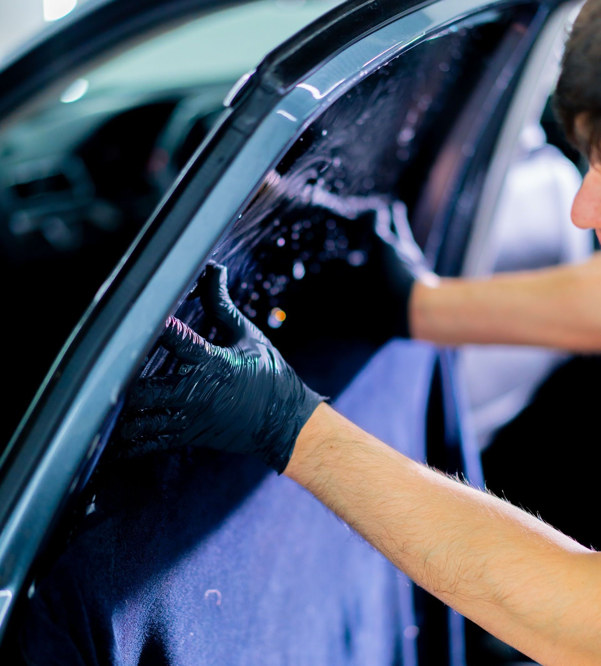 A person wearing black gloves is applying window tint to a car door. They are using their hands to smooth the film.