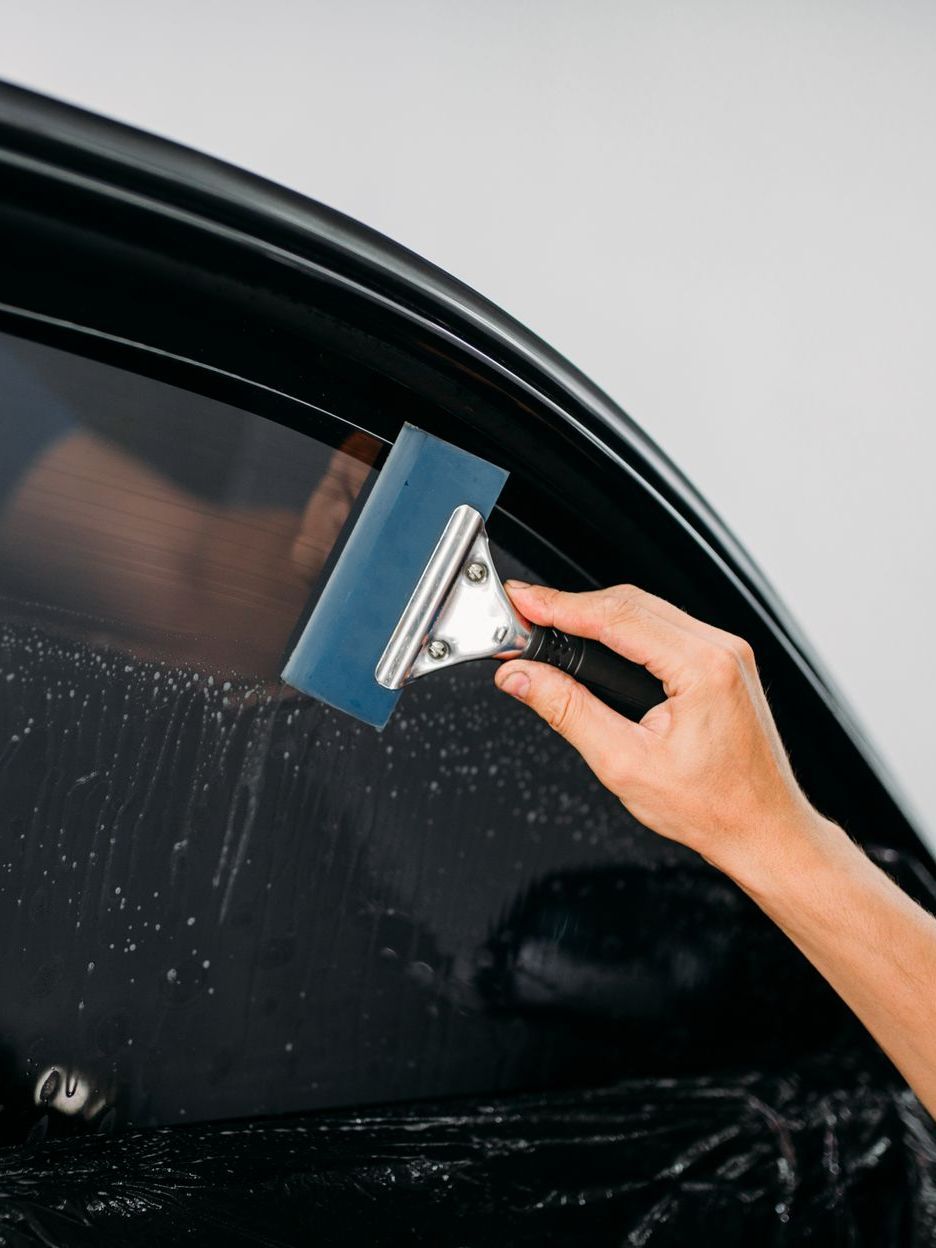 A person applying tinted film to a car window using a squeegee.