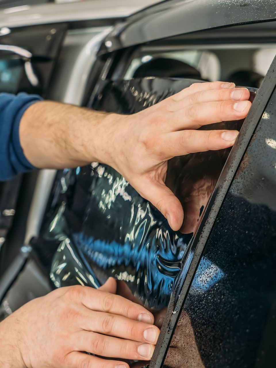 Person applying tinted film to a car window, pressing out bubbles.