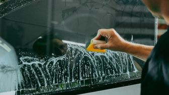 A person applying window tint to a car window with a squeegee, soapy water covering the glass.