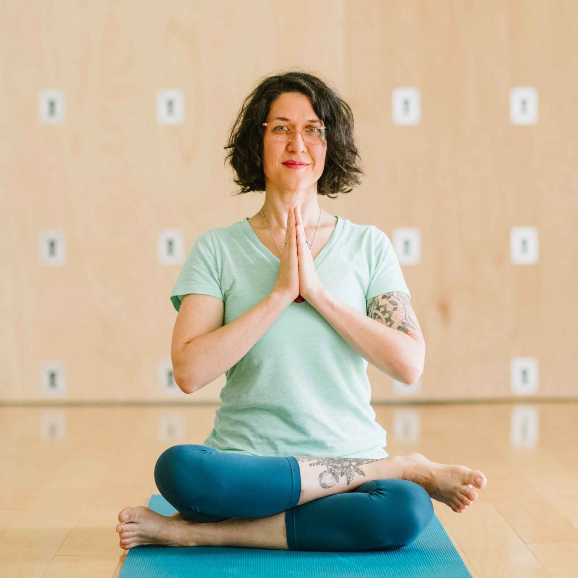 A woman is sitting on a yoga mat with her hands folded in prayer.