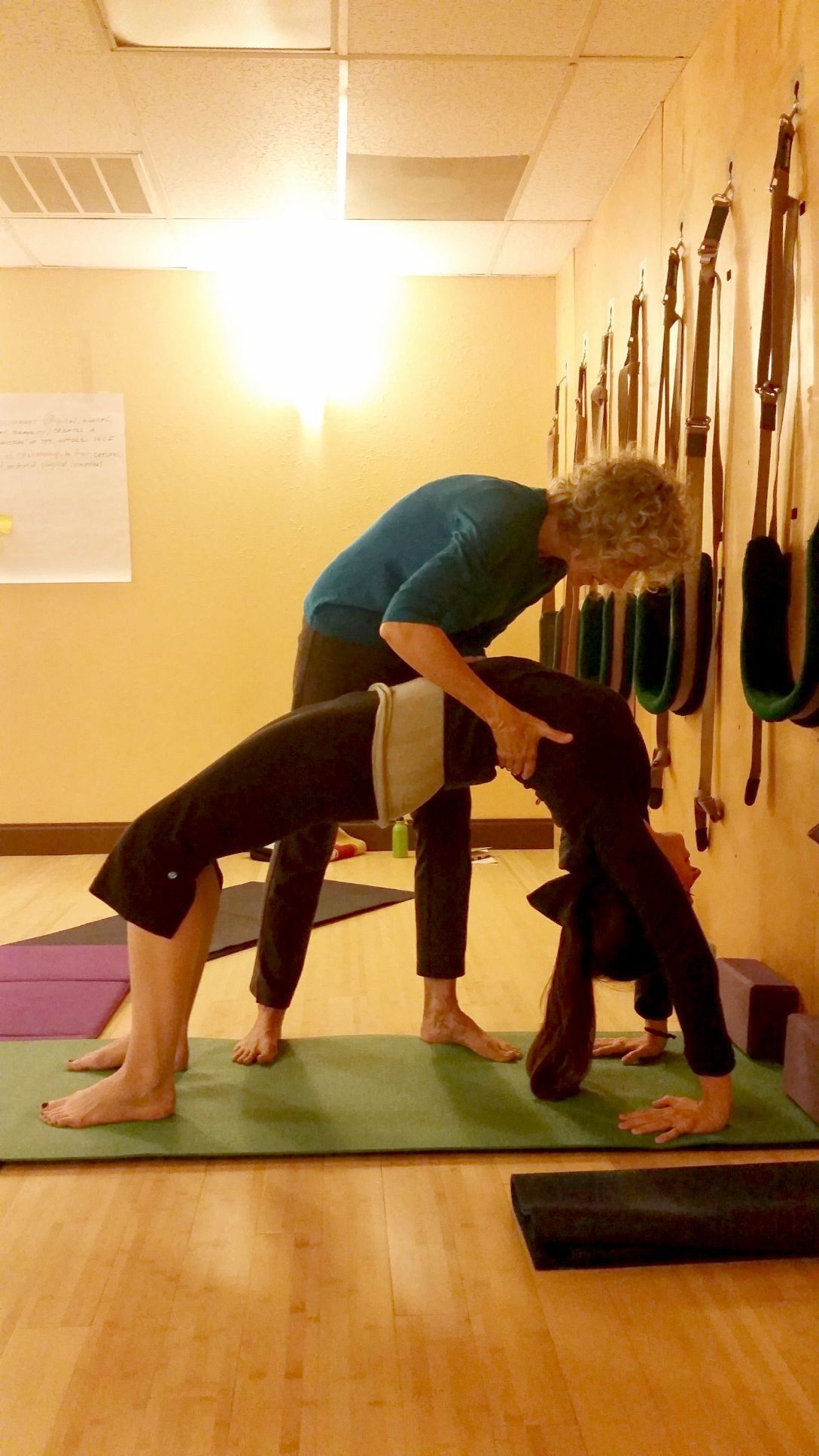 A woman is helping another woman do a Pilates pose on a mat.