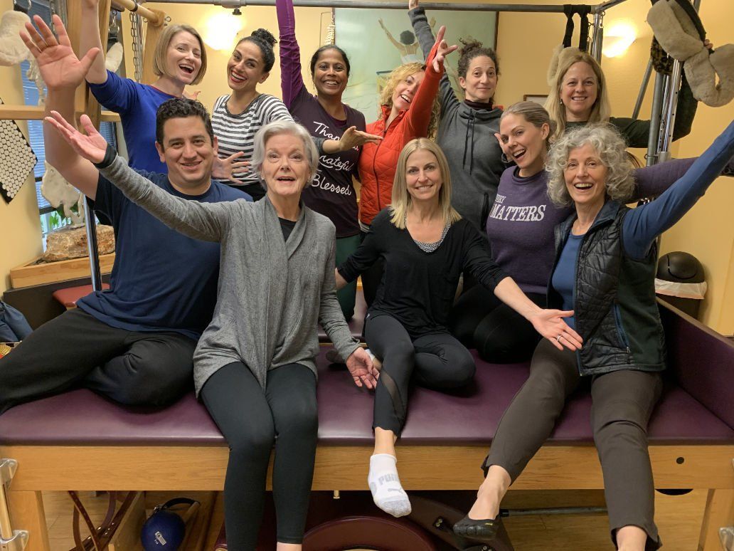 A group of people are sitting on a Pilates cadillac with their arms in the air.