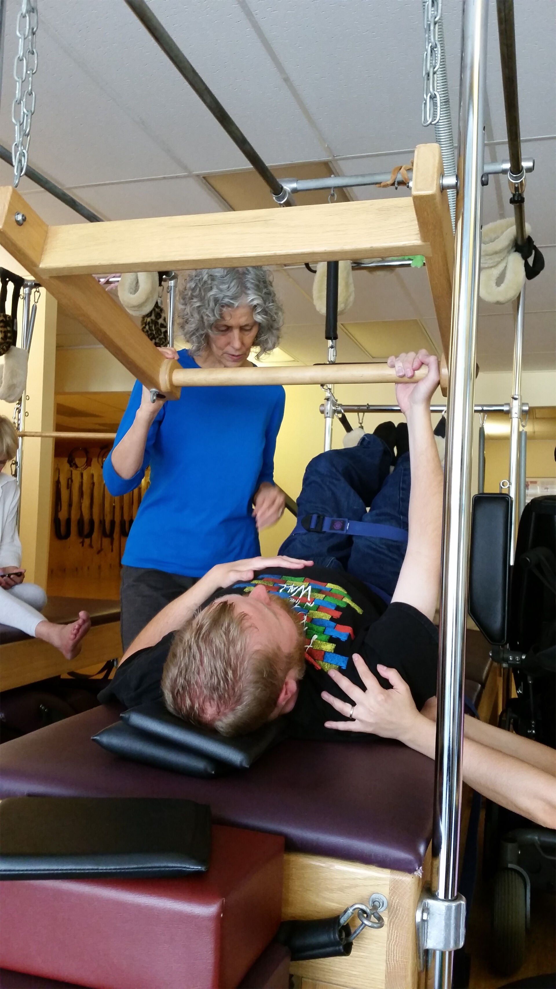 A woman is helping a man do exercises on a pilates machine.