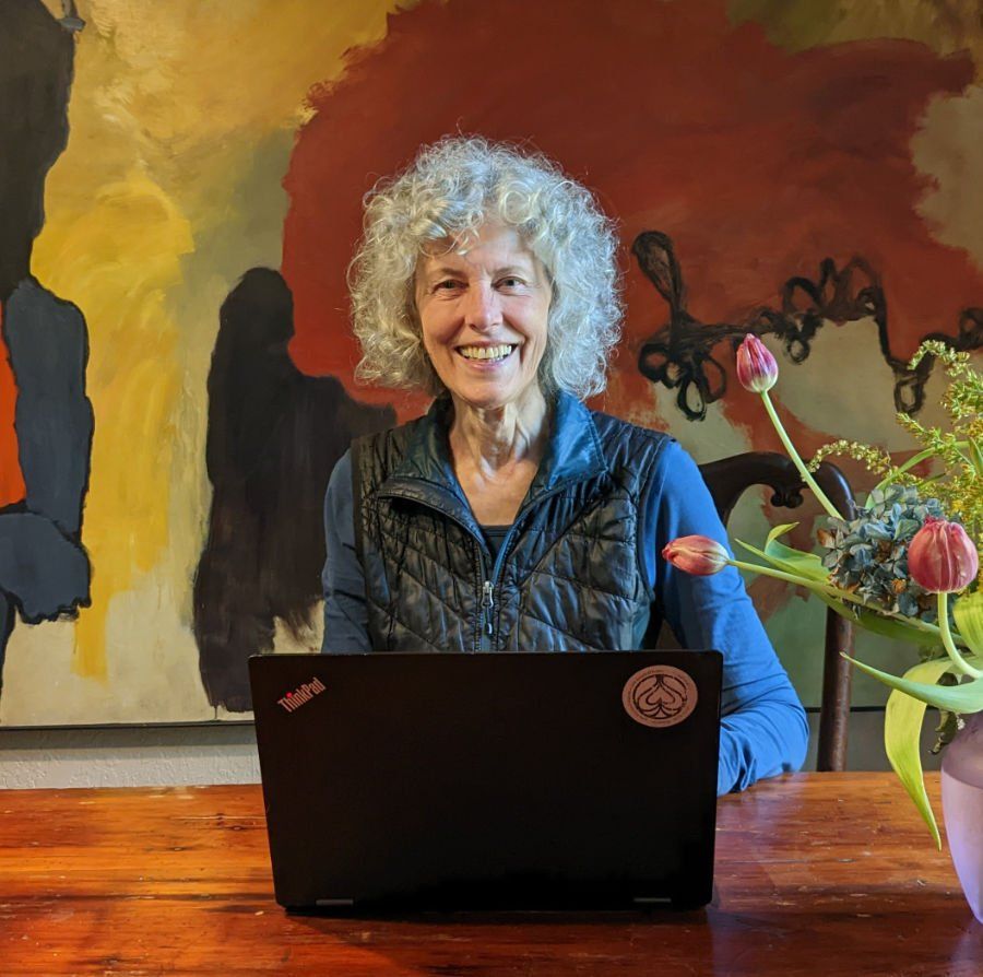 A woman is sitting at a table with a laptop and smiling